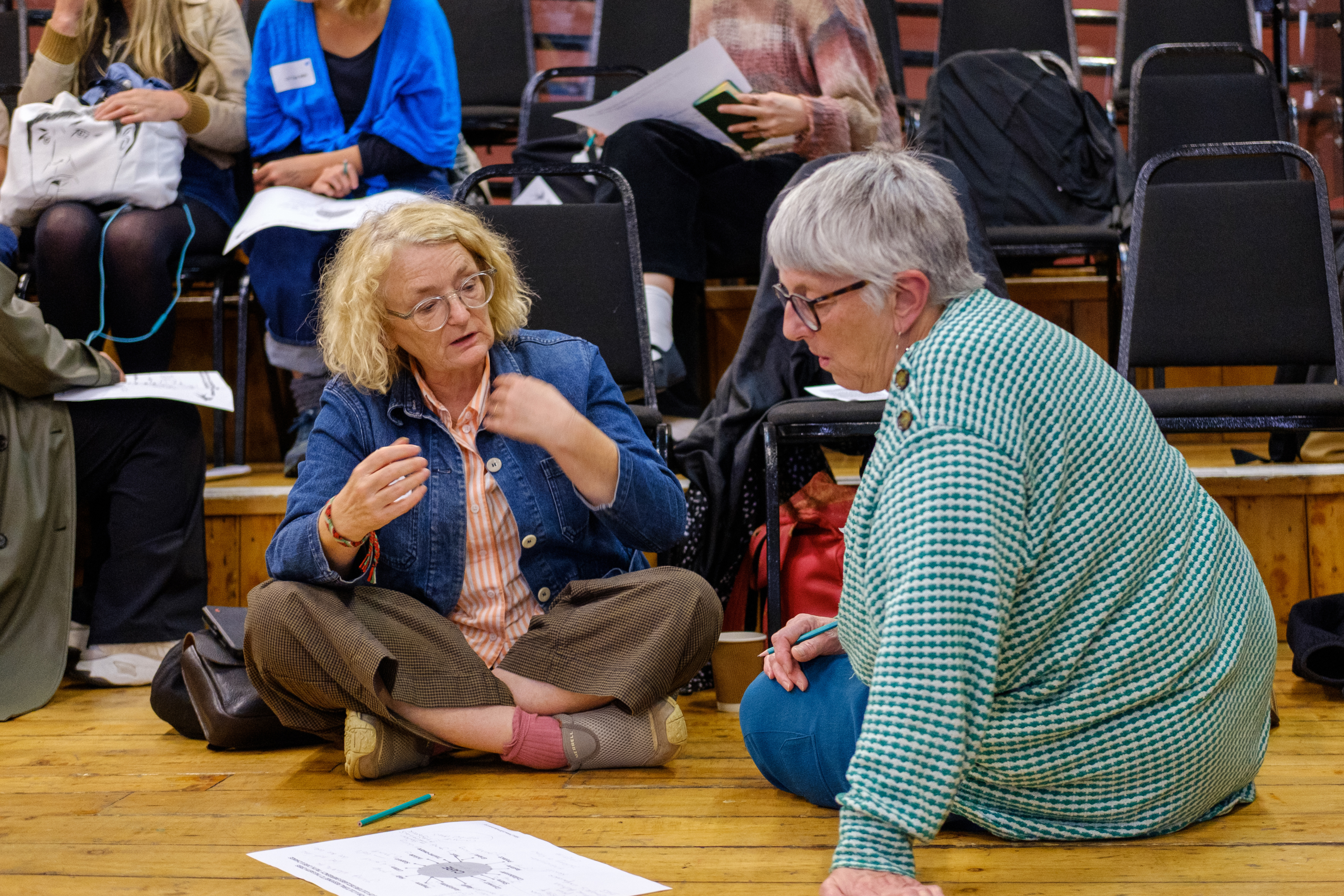 Two people sitting on a wooden floor looking at a piece of paper.