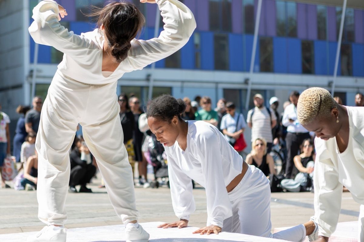 Three dancers in white outfits dancing in different positions on a stage in front of a large audience.
