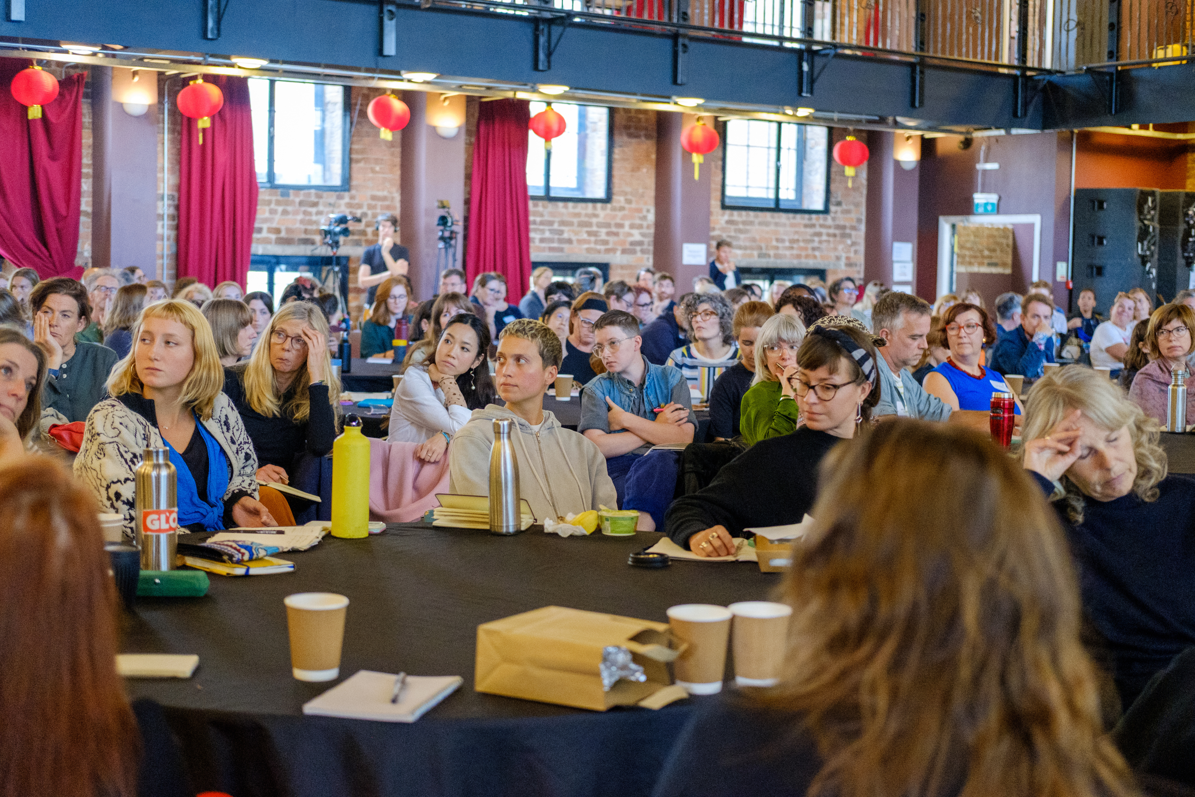 A large room full of people sitting around big circular tables.
