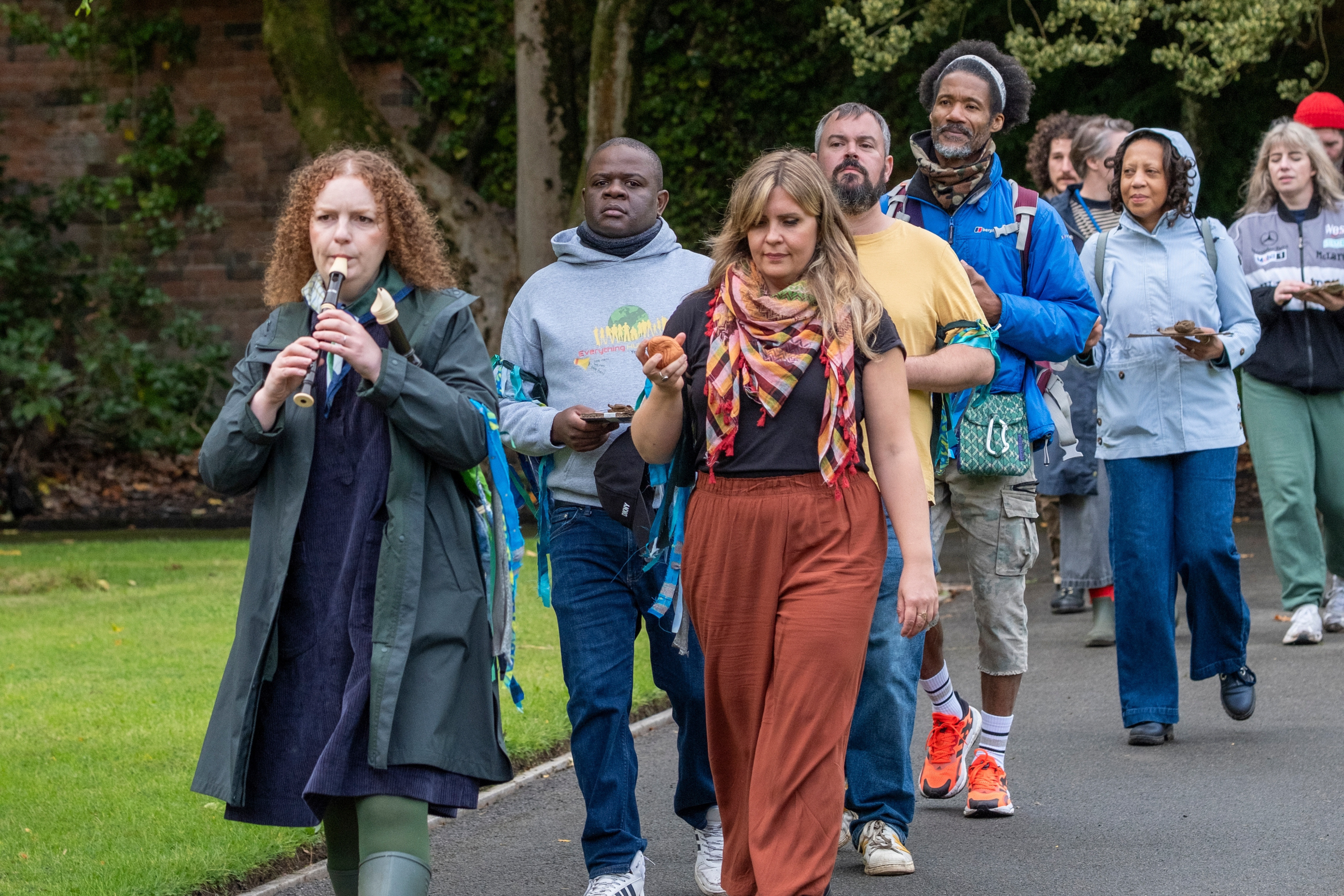 A woman playing a recorder leads a procession of people through a garden