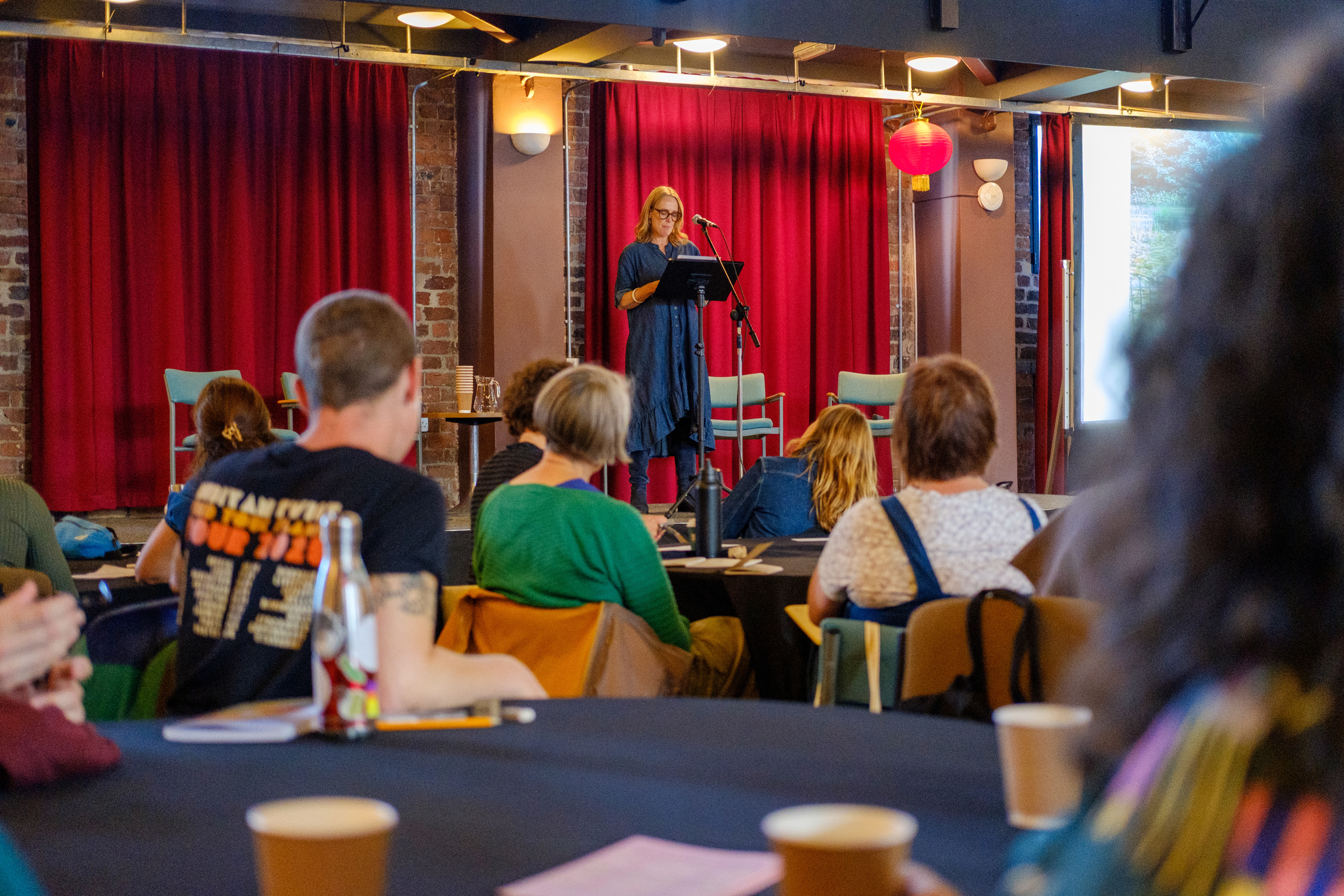Emma Underhill standing on a stage with large red curtains behind a microphone stand.