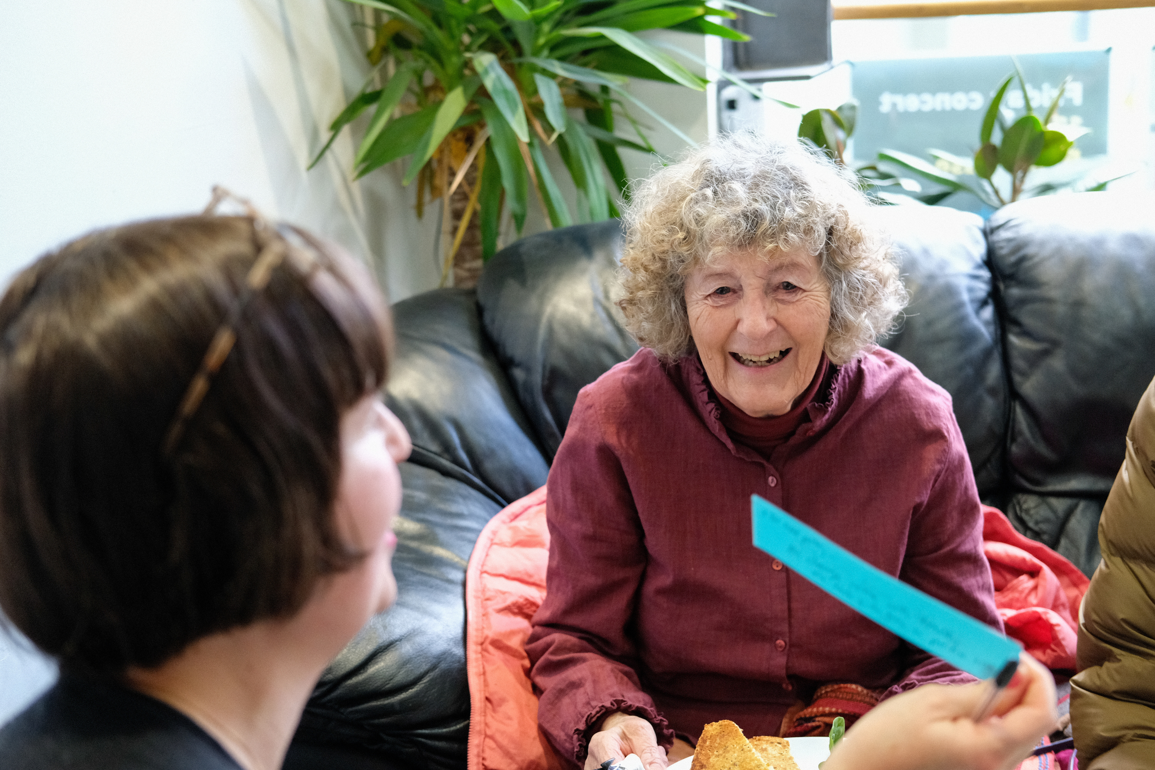 Two women in conversation around a sofa looking at a slip of paper.
