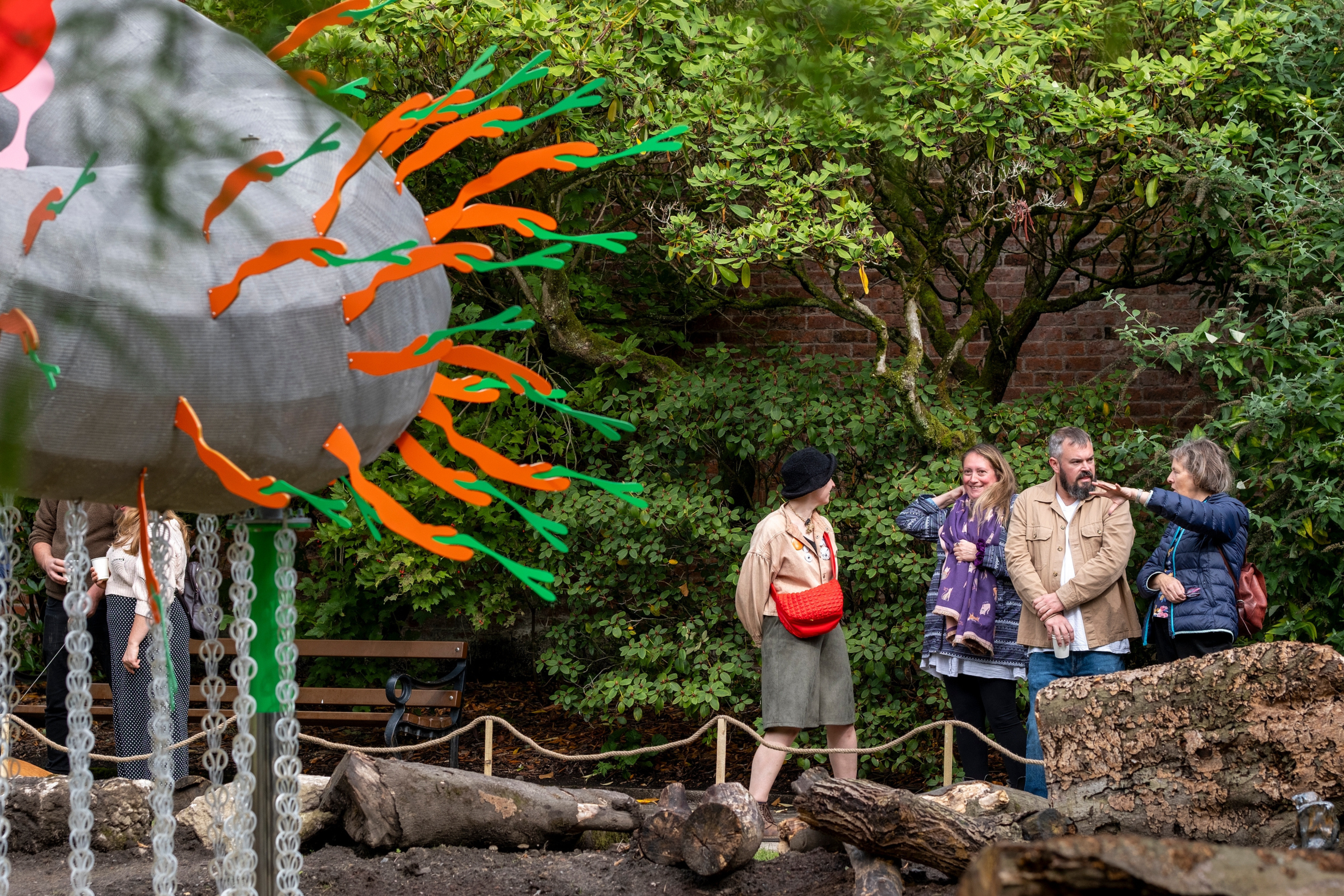 A group of people standing in front of a large metal sculpture with green and orange snake-like points sticking out.