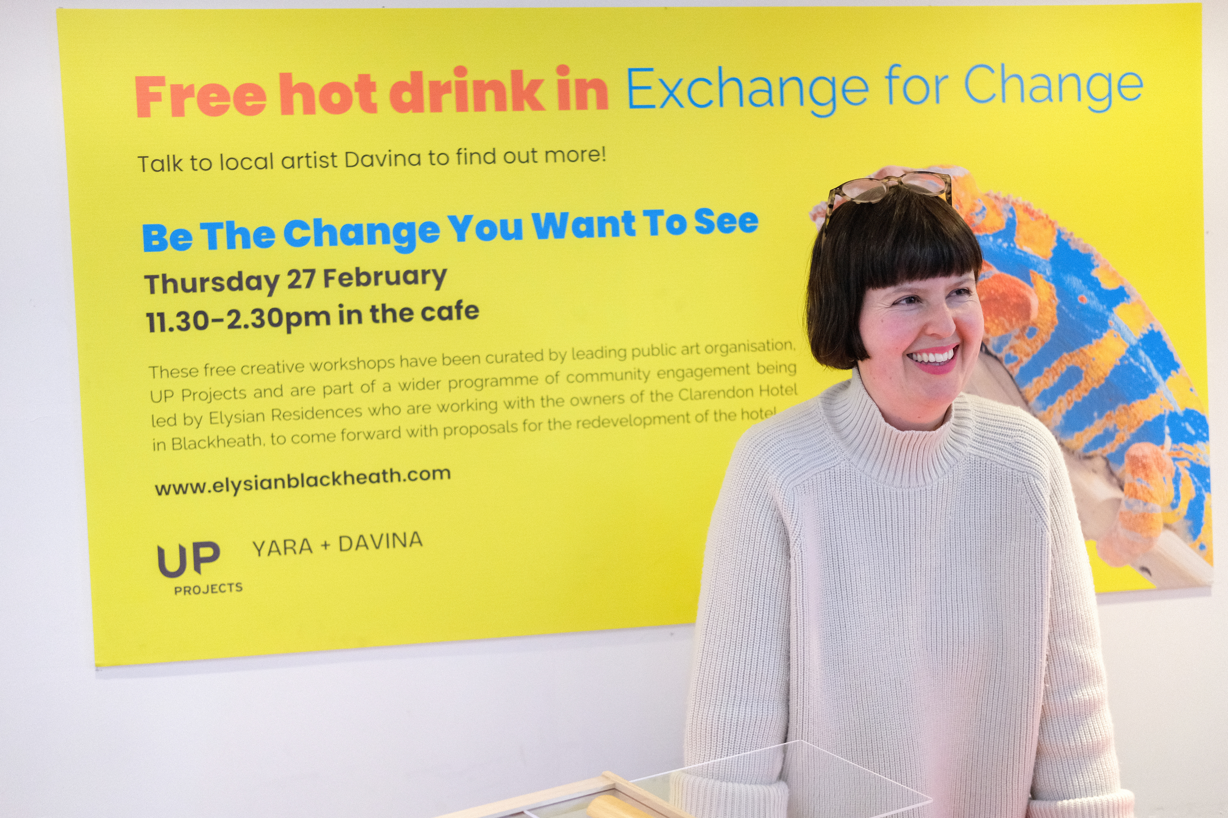 Davina Drummond smiling stood in front of a sign that says 'Free Hot Drink in exchange for Change'