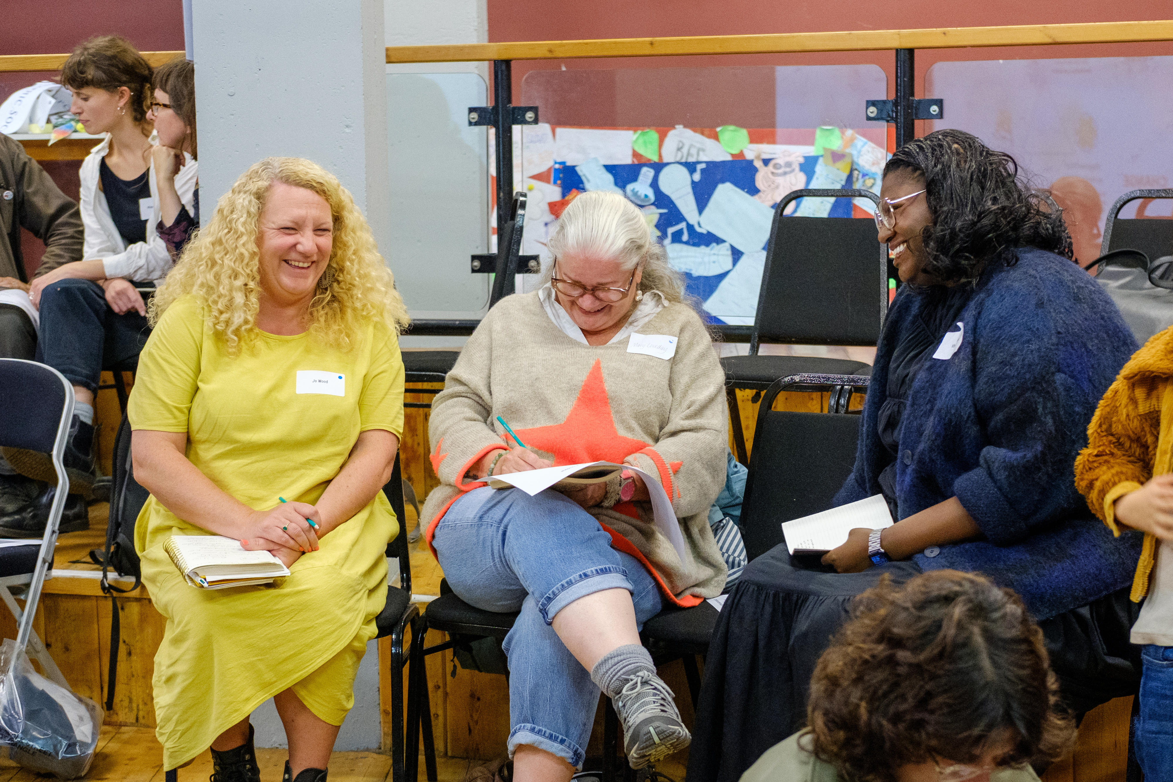 Three people sitting on chairs in a row all smiling.
