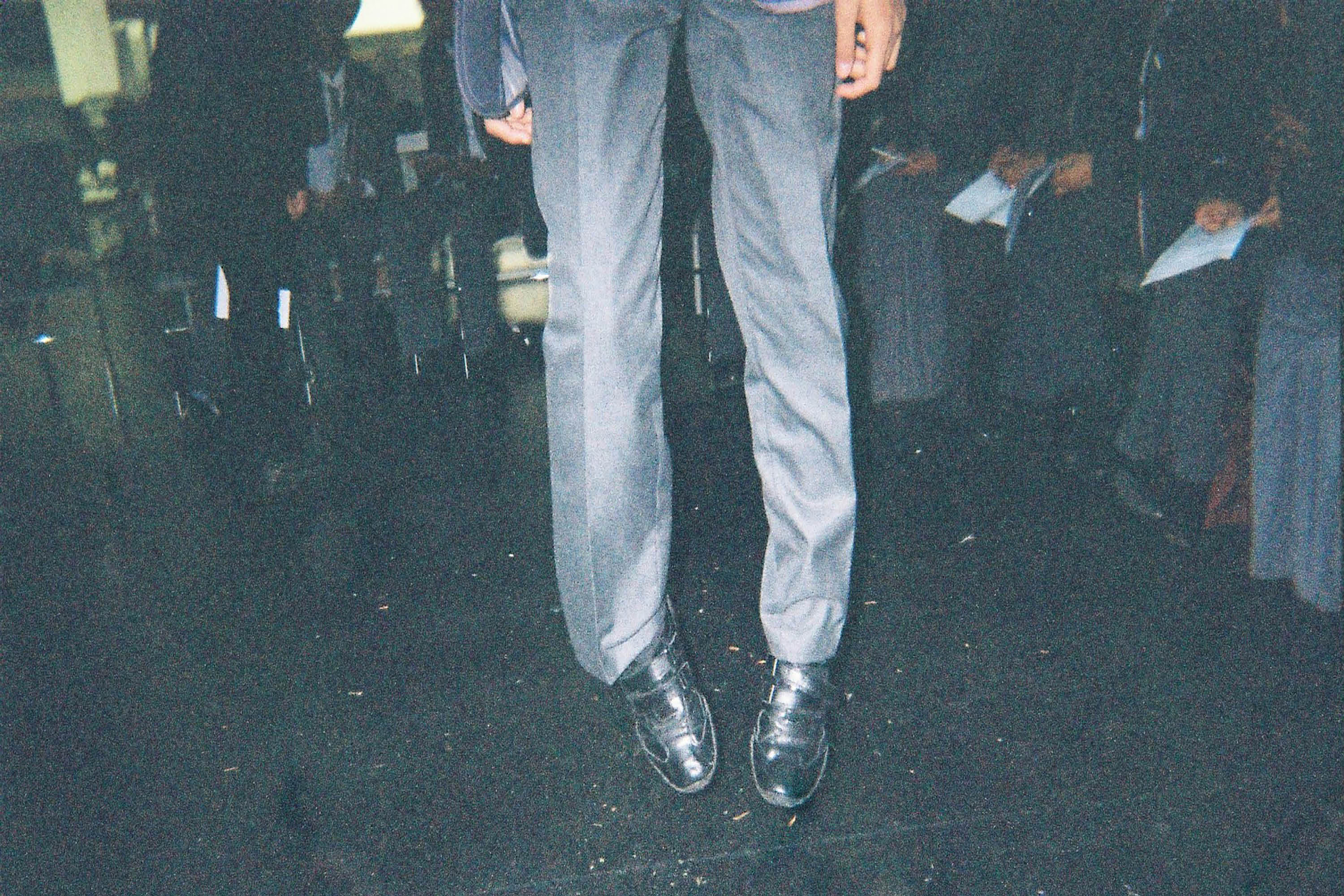 A low angle photograph of a male standing in suit trousers in the middle of a seated crowd.