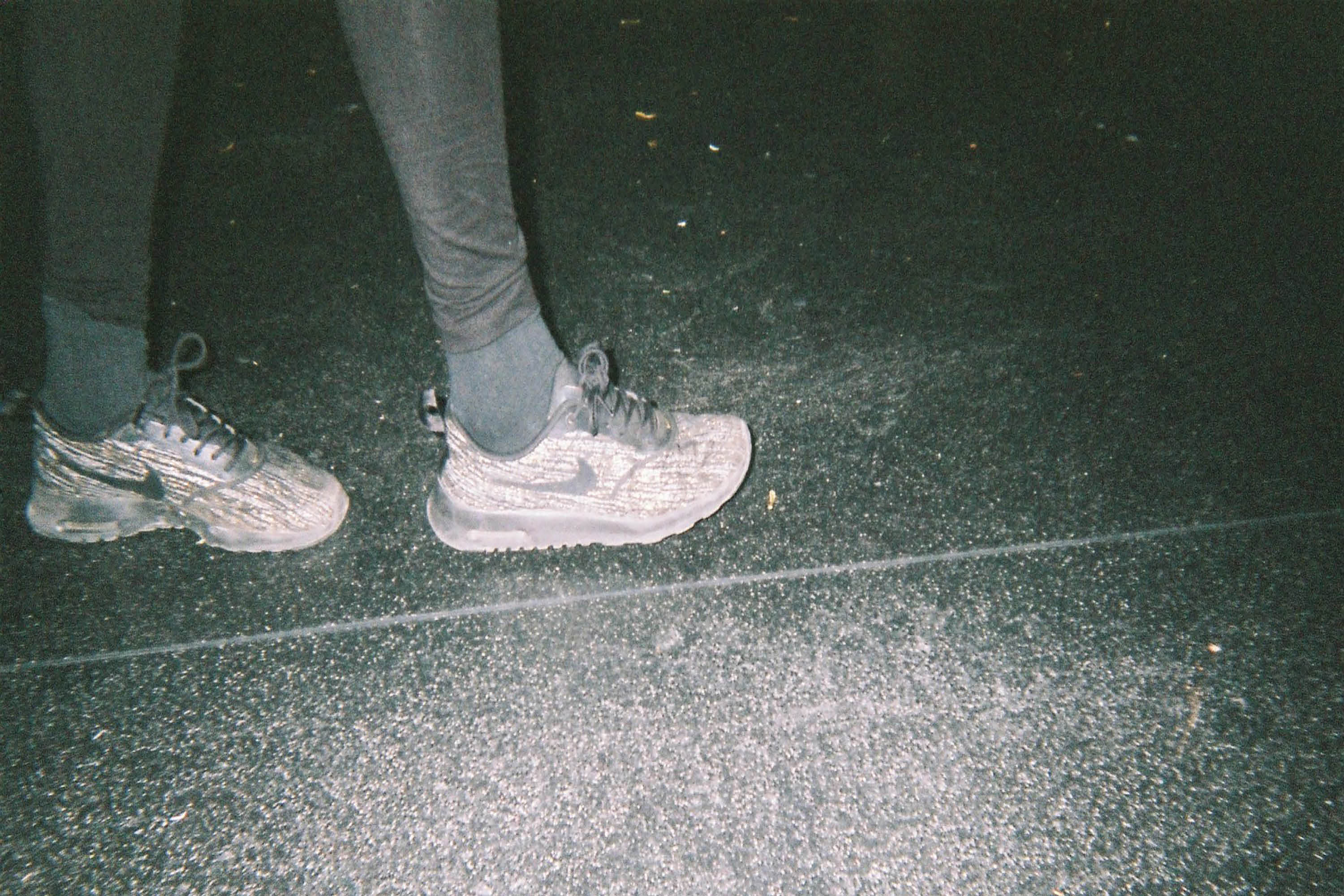 A low angle of person wearing white Nike Trainers walking across an unclean dark grey floor.