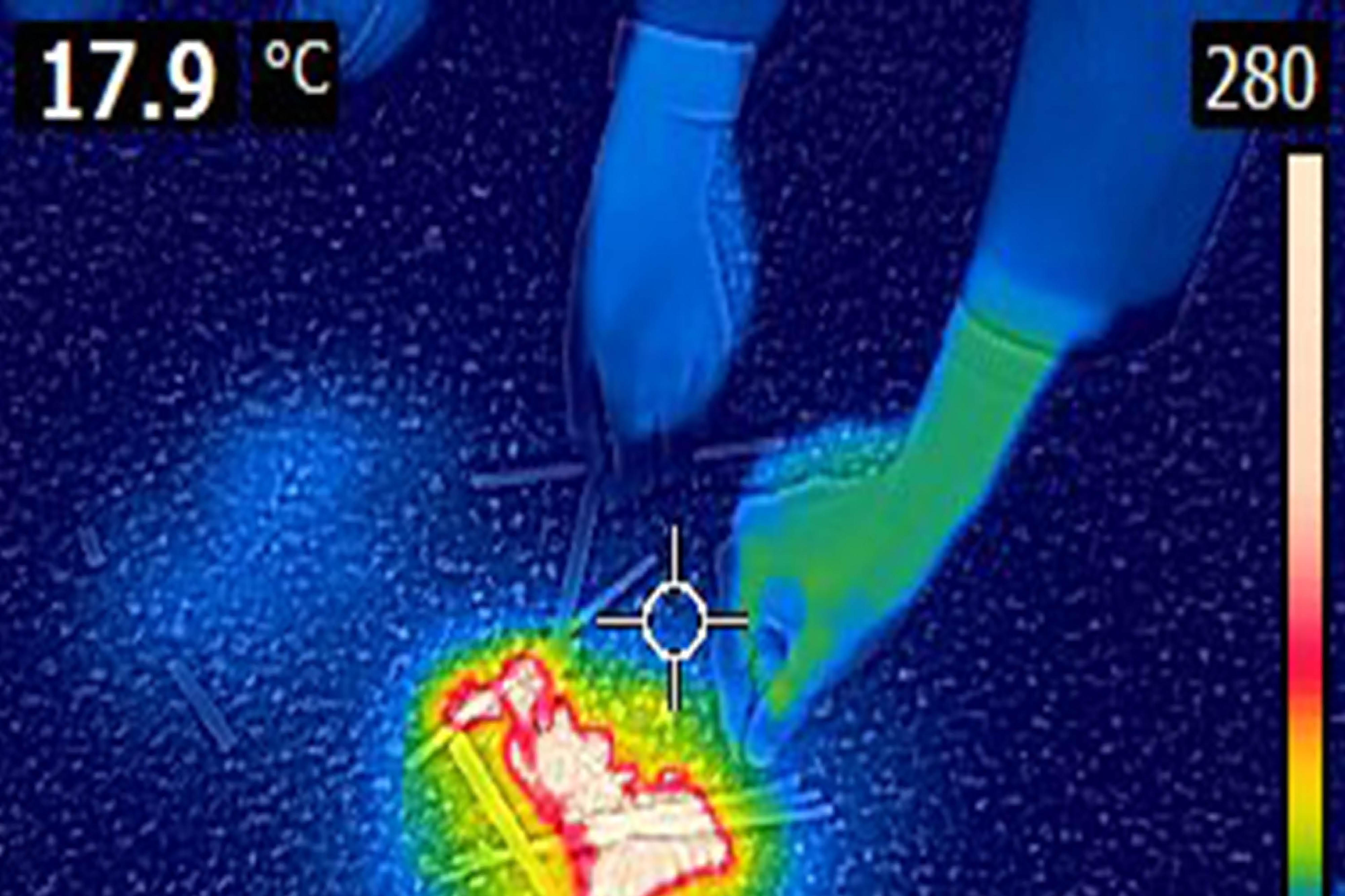 A thermographic photograph of two people moving sticks into a small fire.