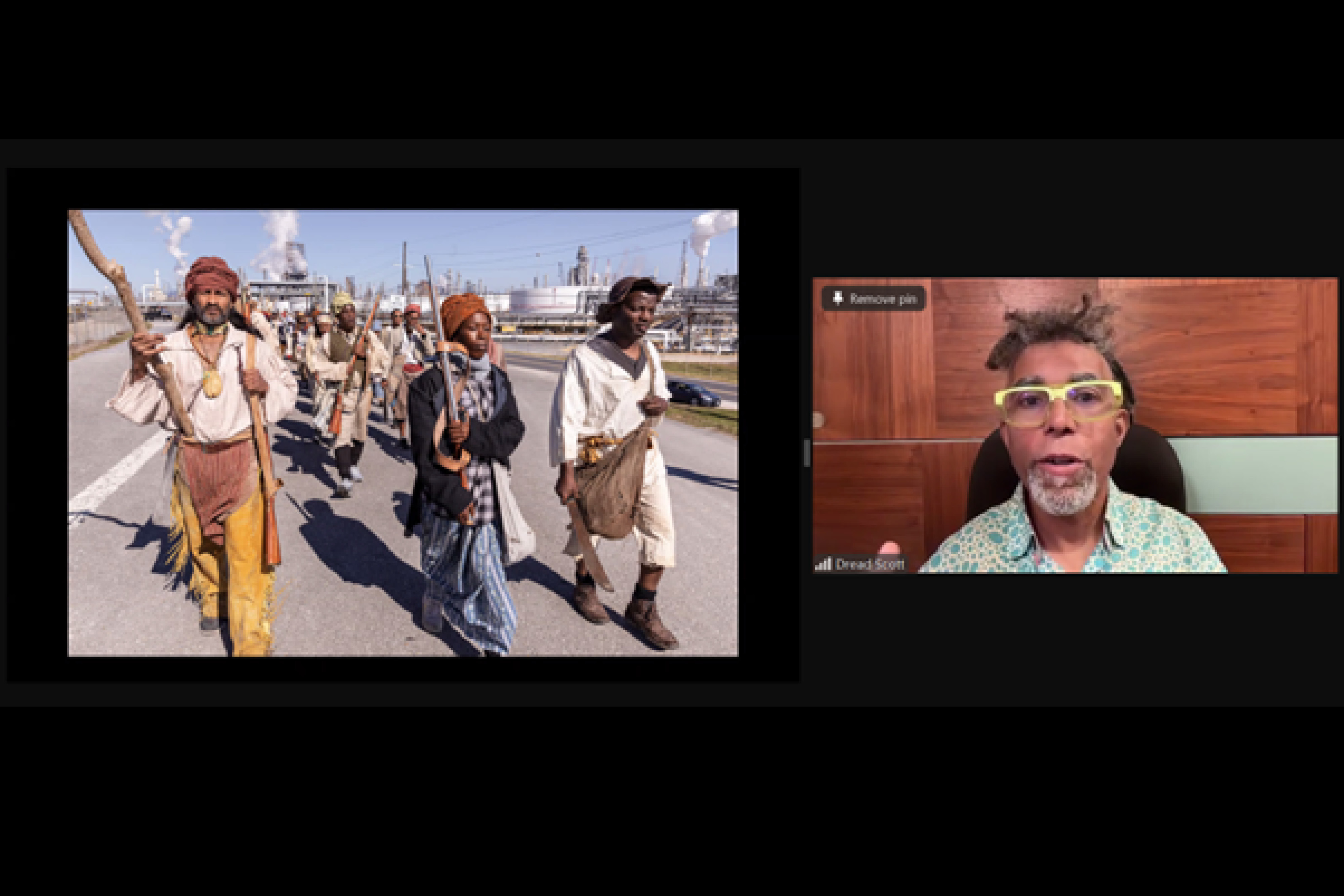 A man speaking on a zoom call. The image next to him shows a group of people dressed in re-enactment costumes on a road.
