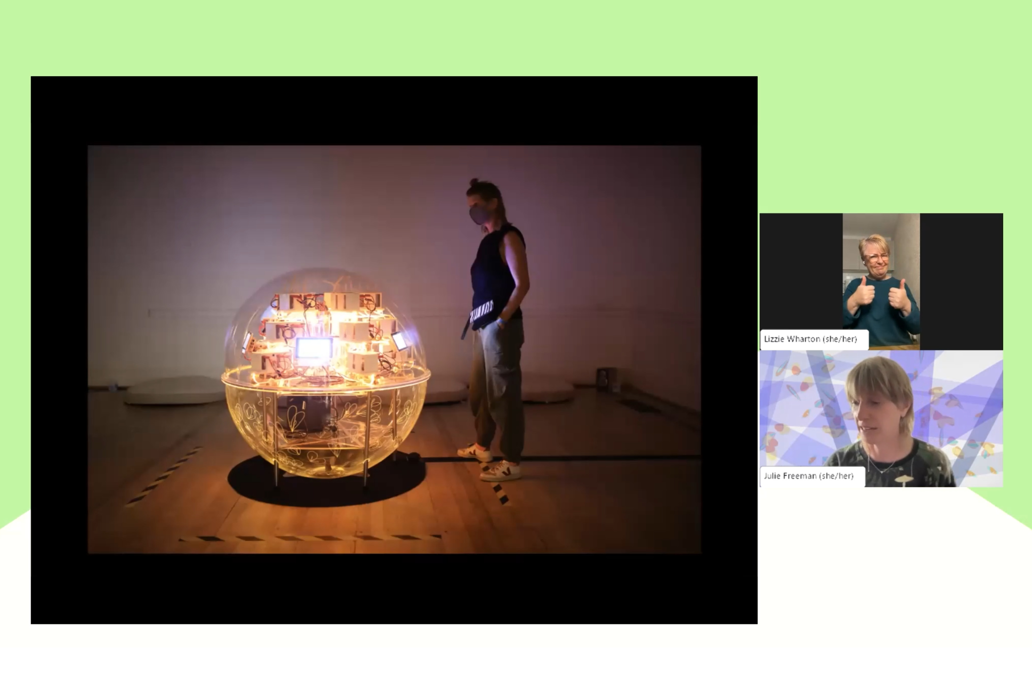 Two people on a zoom call. The image next to them shows a person in a gallery next to a large circular ball containing many lights.