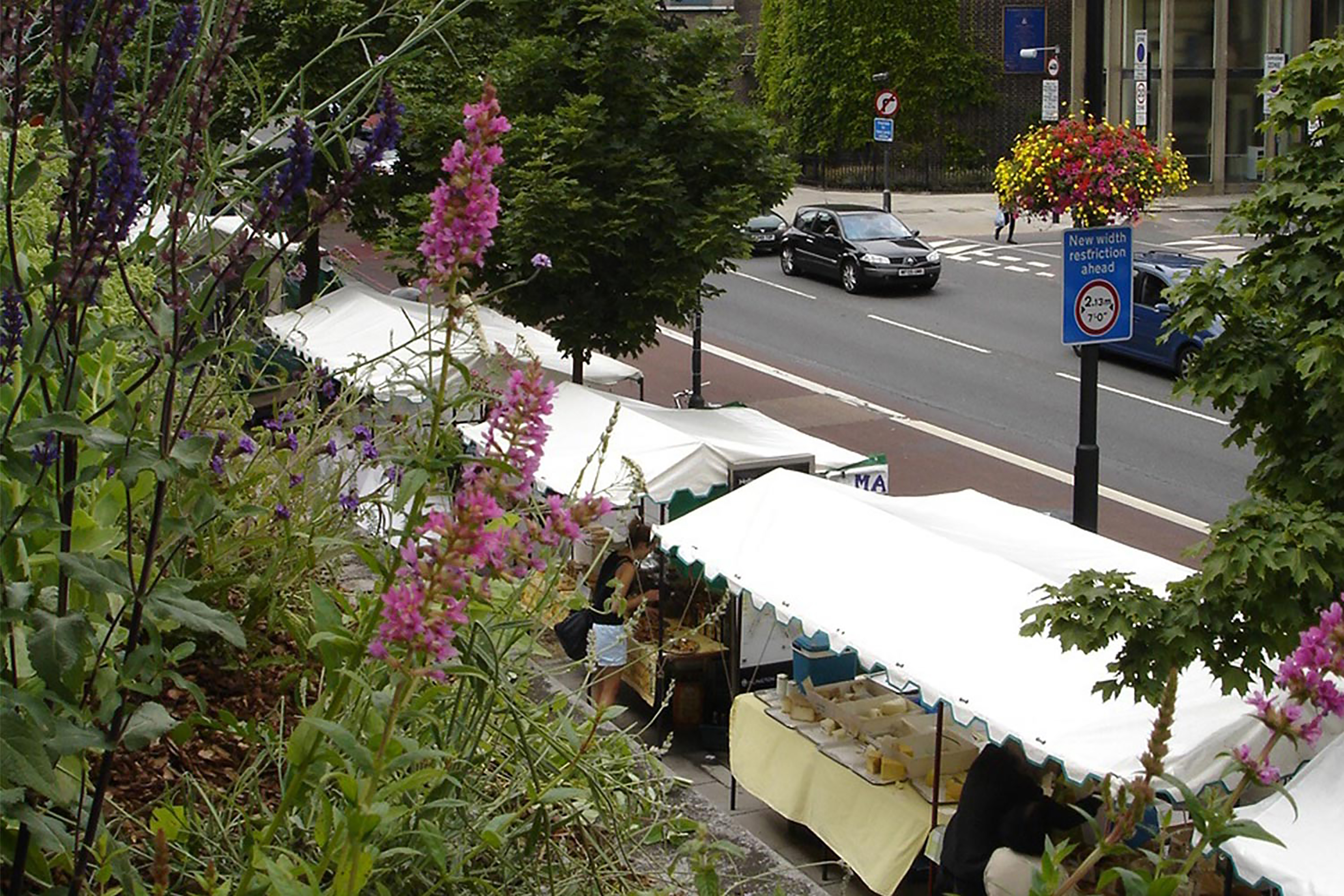 A photograph of farmers market stalls next to a busy road..