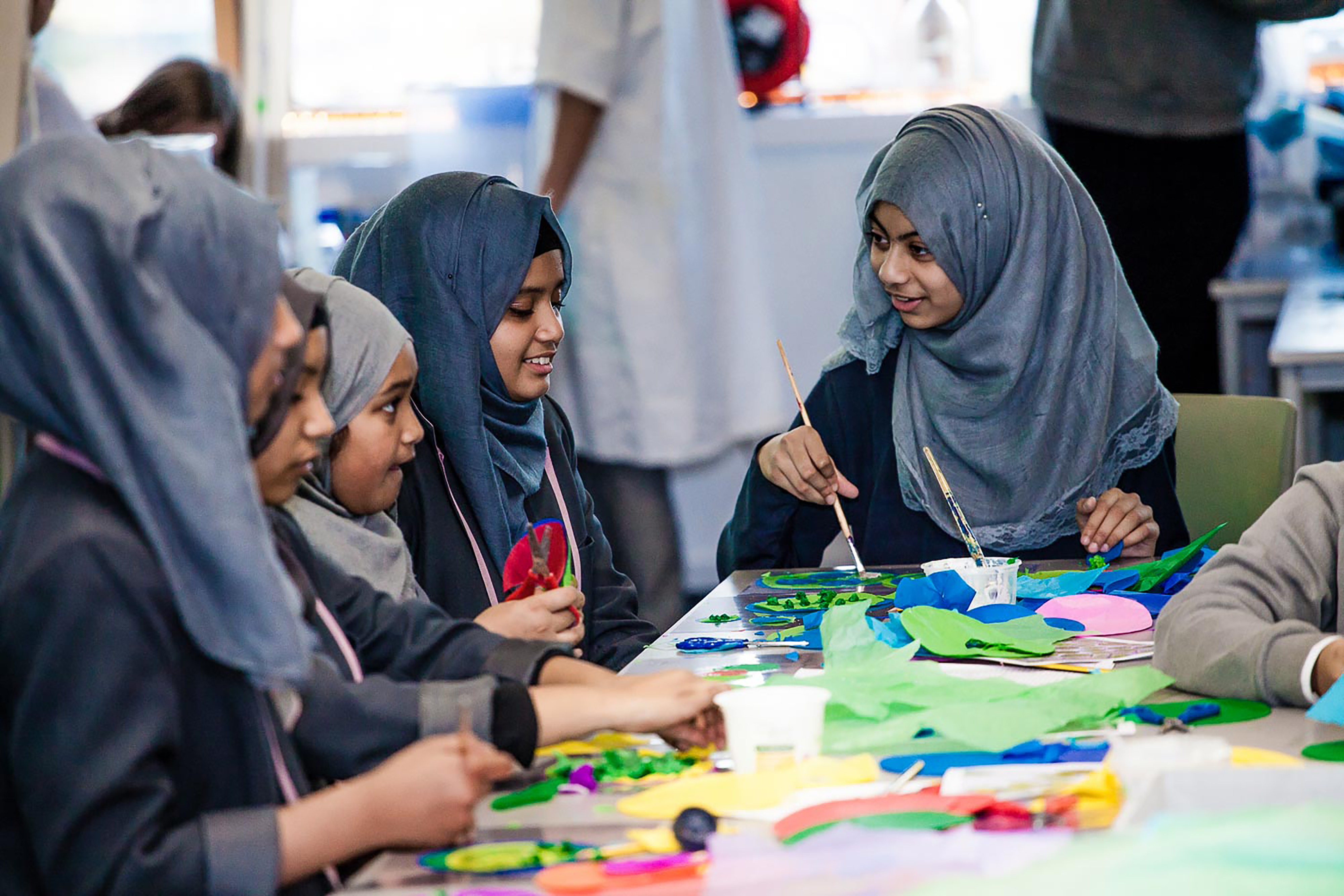 A group of school girls painting and handcrafting items in a classroom.