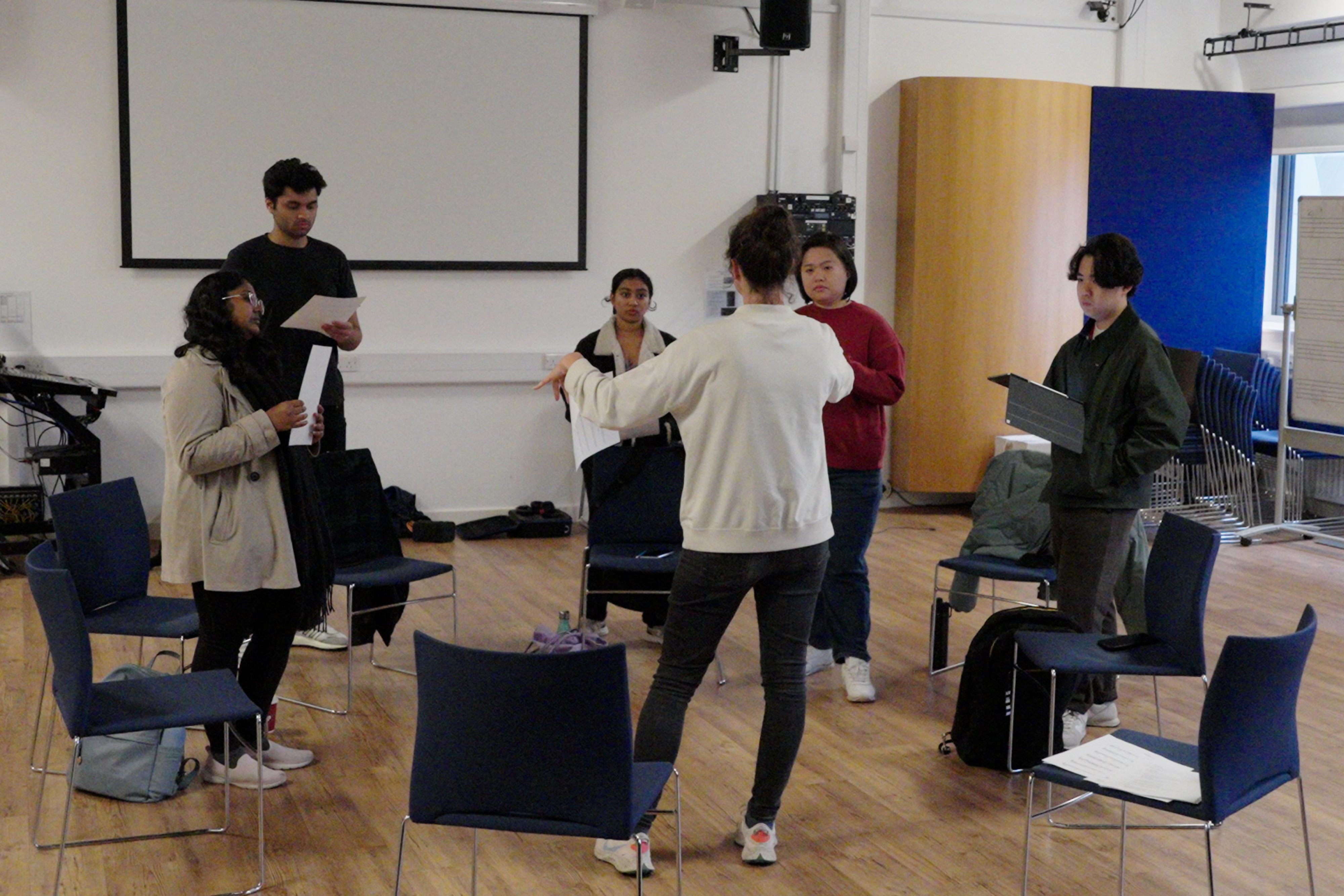 A group of people in a circle holding music sheets singing in a large room.