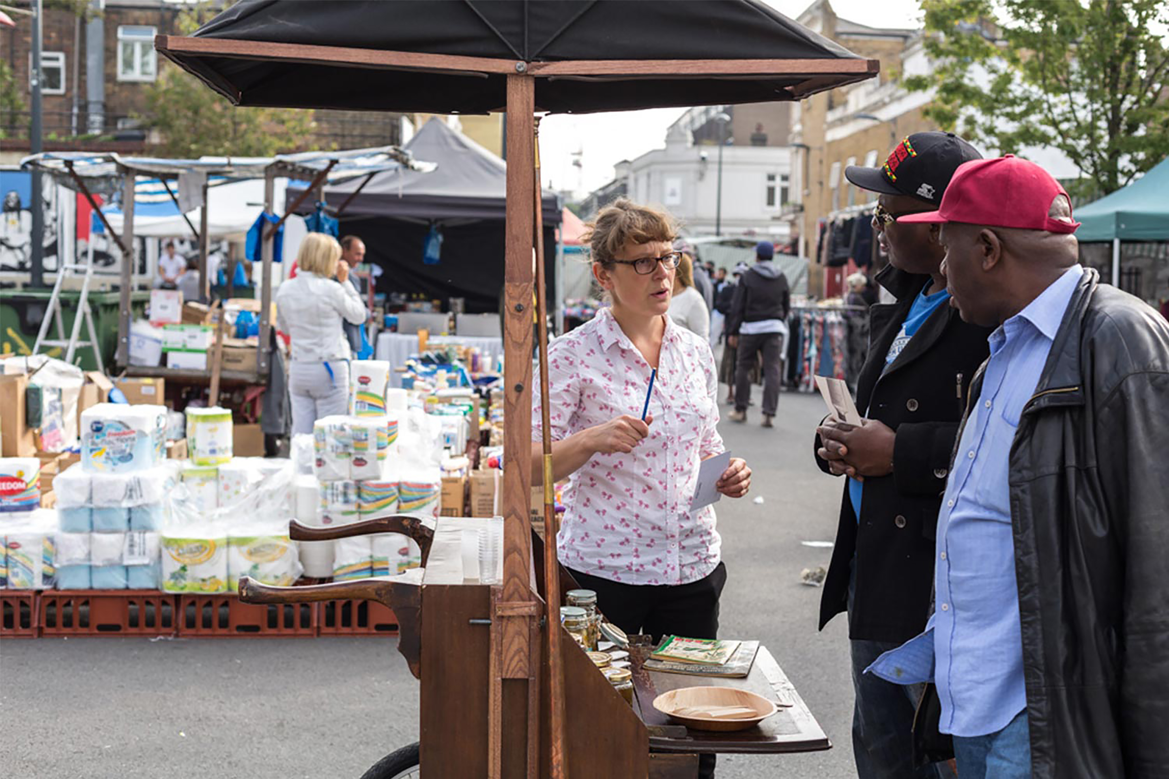 A group of people standing in front of a wooden food stand full of different types of products.