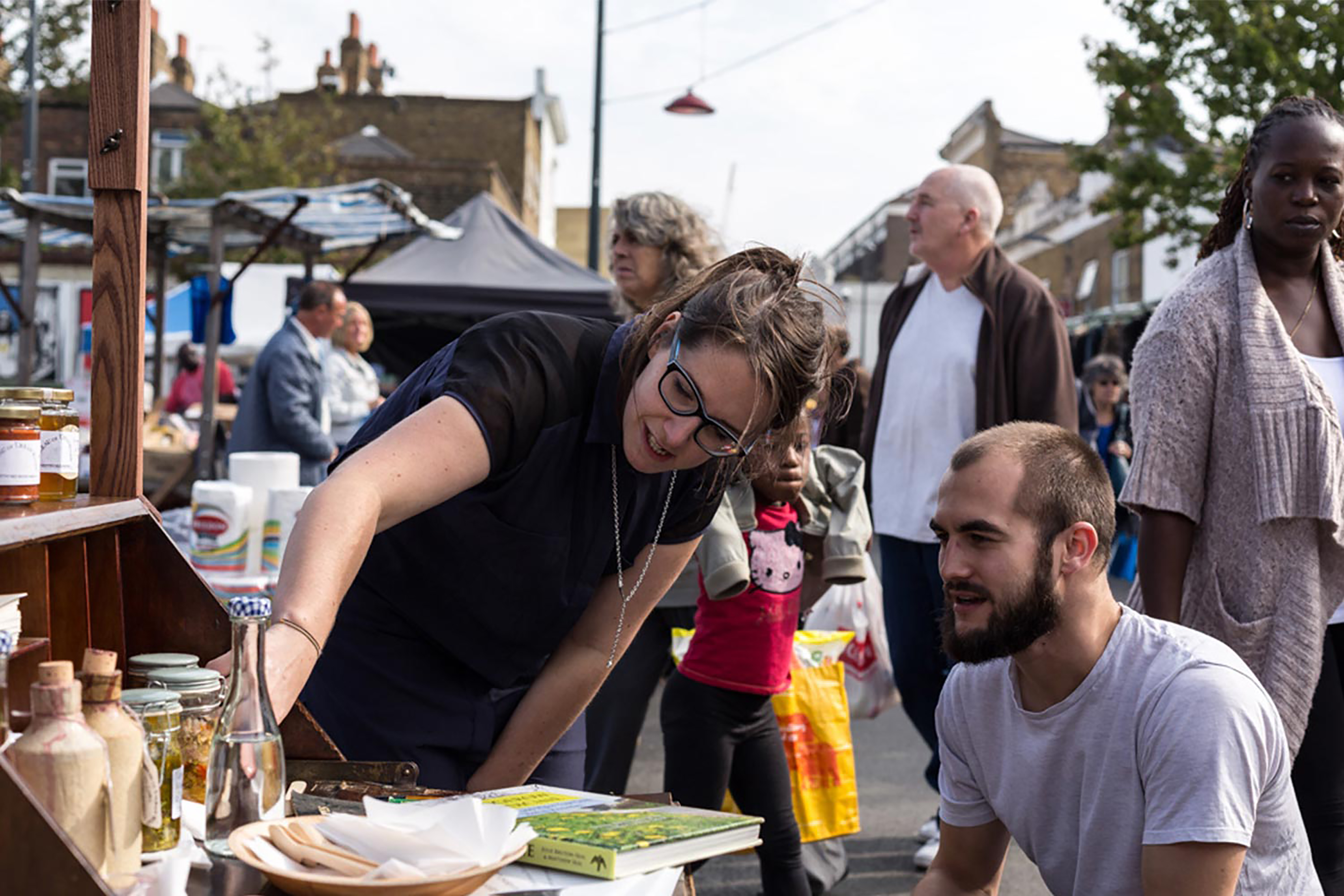 A group of people standing in front of a wooden food stand full of different types of products.