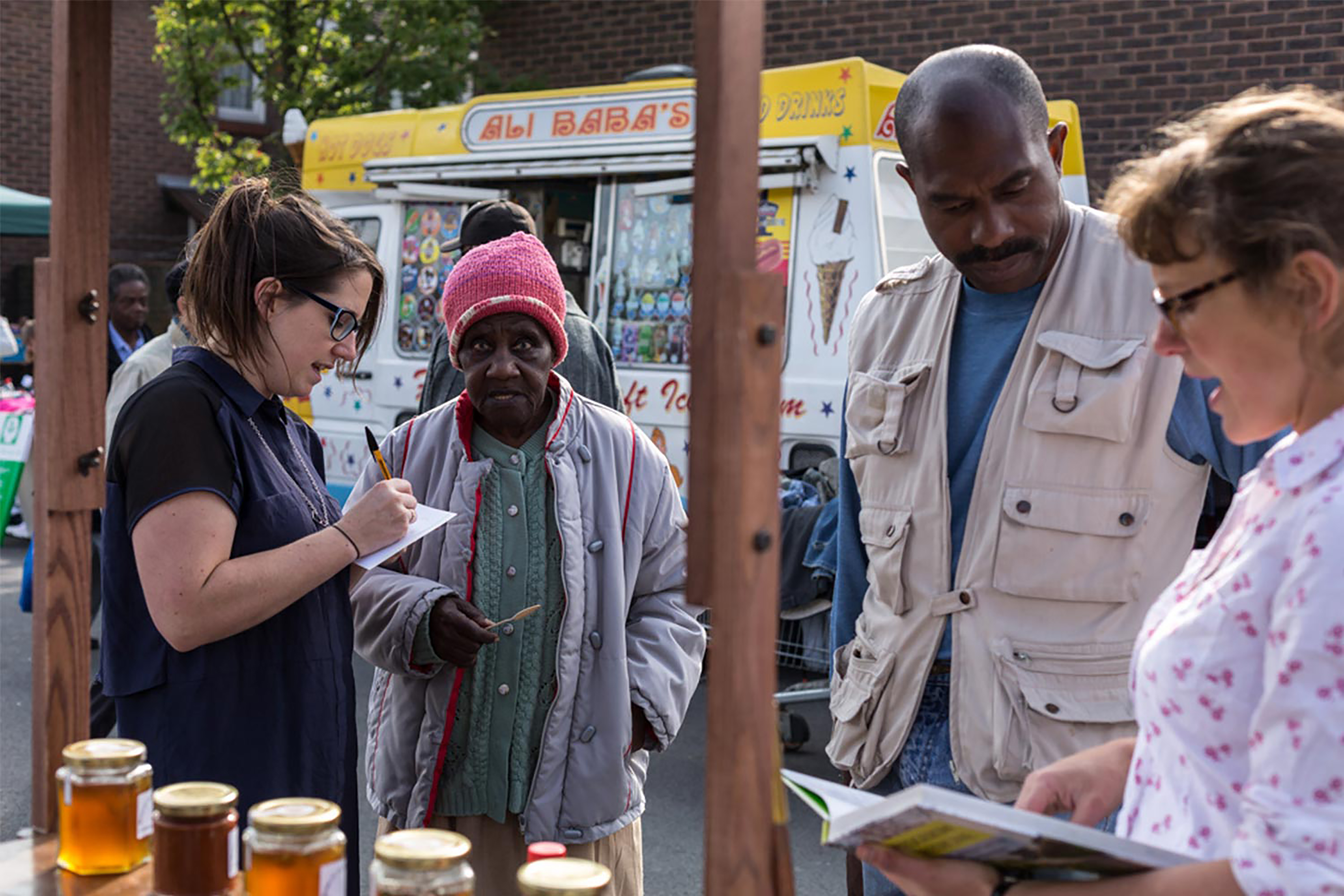 A group of people standing in front of a wooden food stand with an ice cream van in the background.