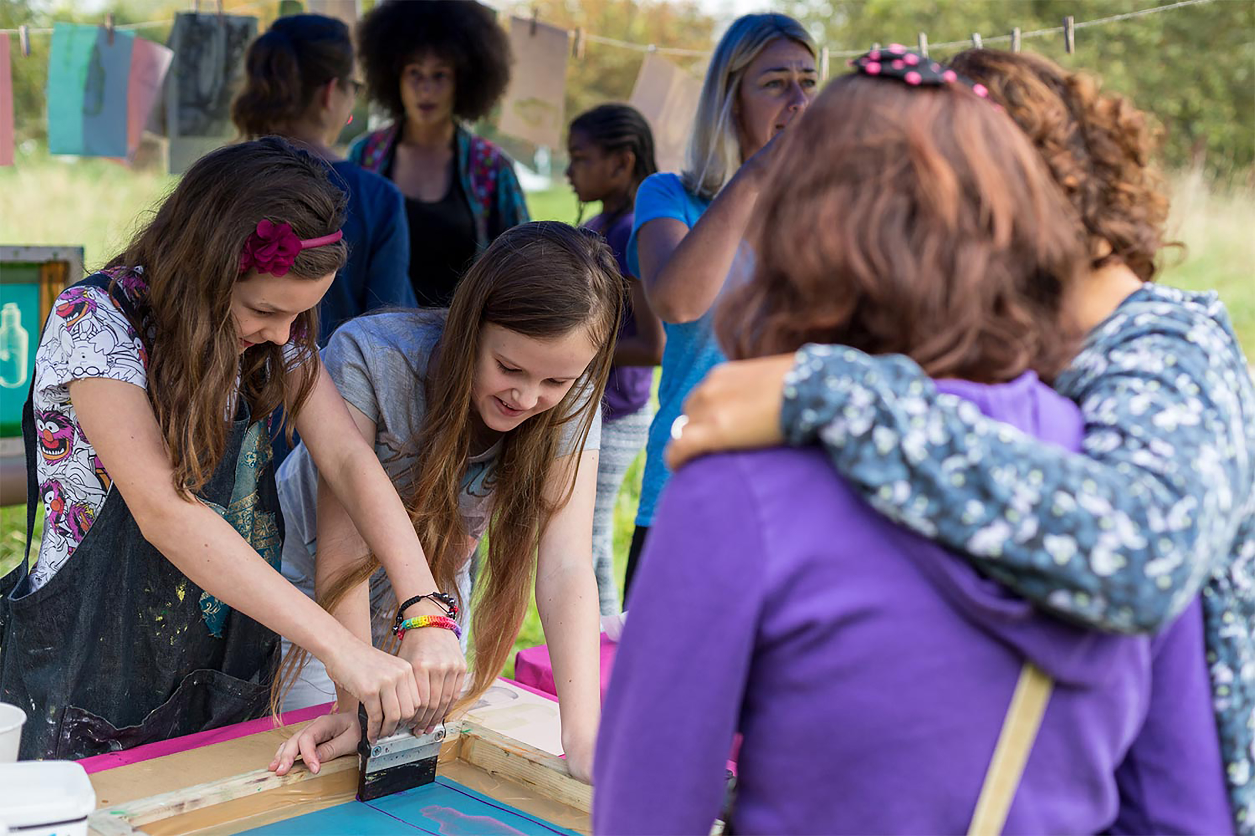 Two young girls screen printing surrounded by a group of people.