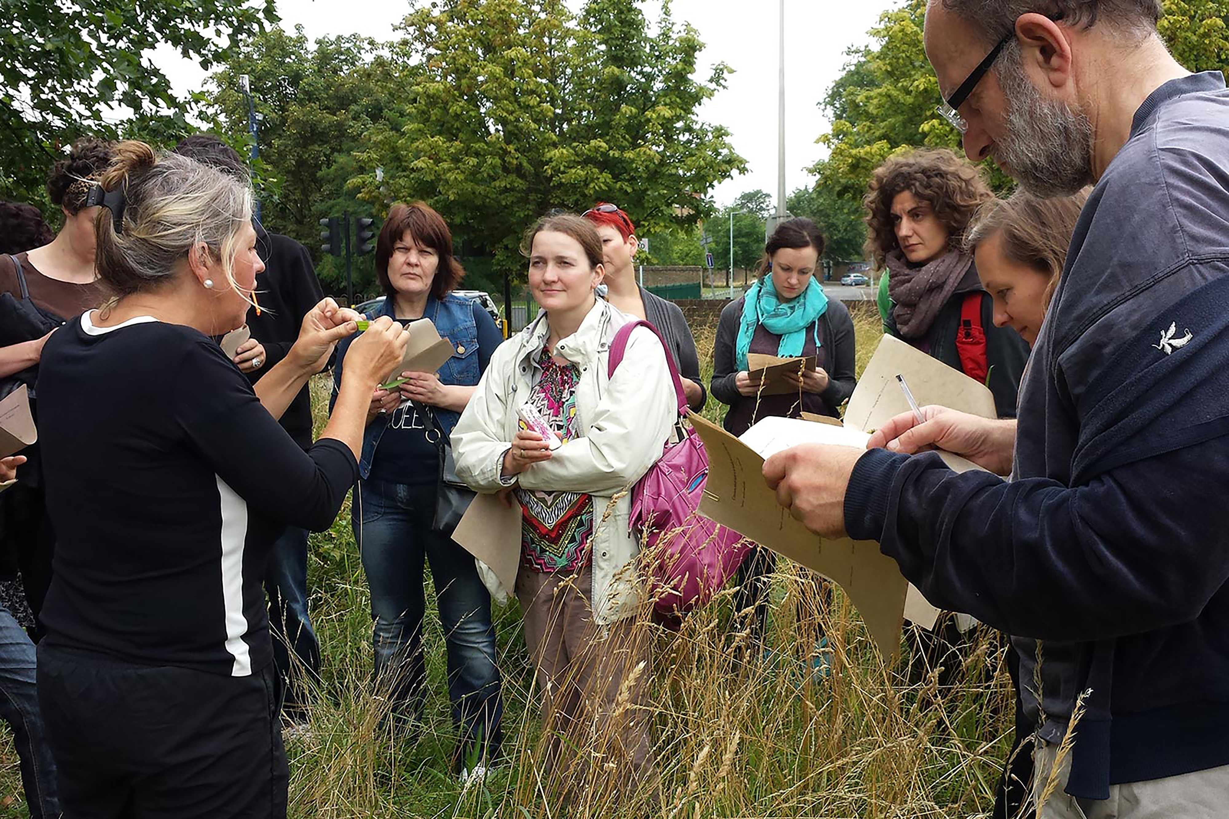 A group of people huddled together listening to a woman speaking in a field.