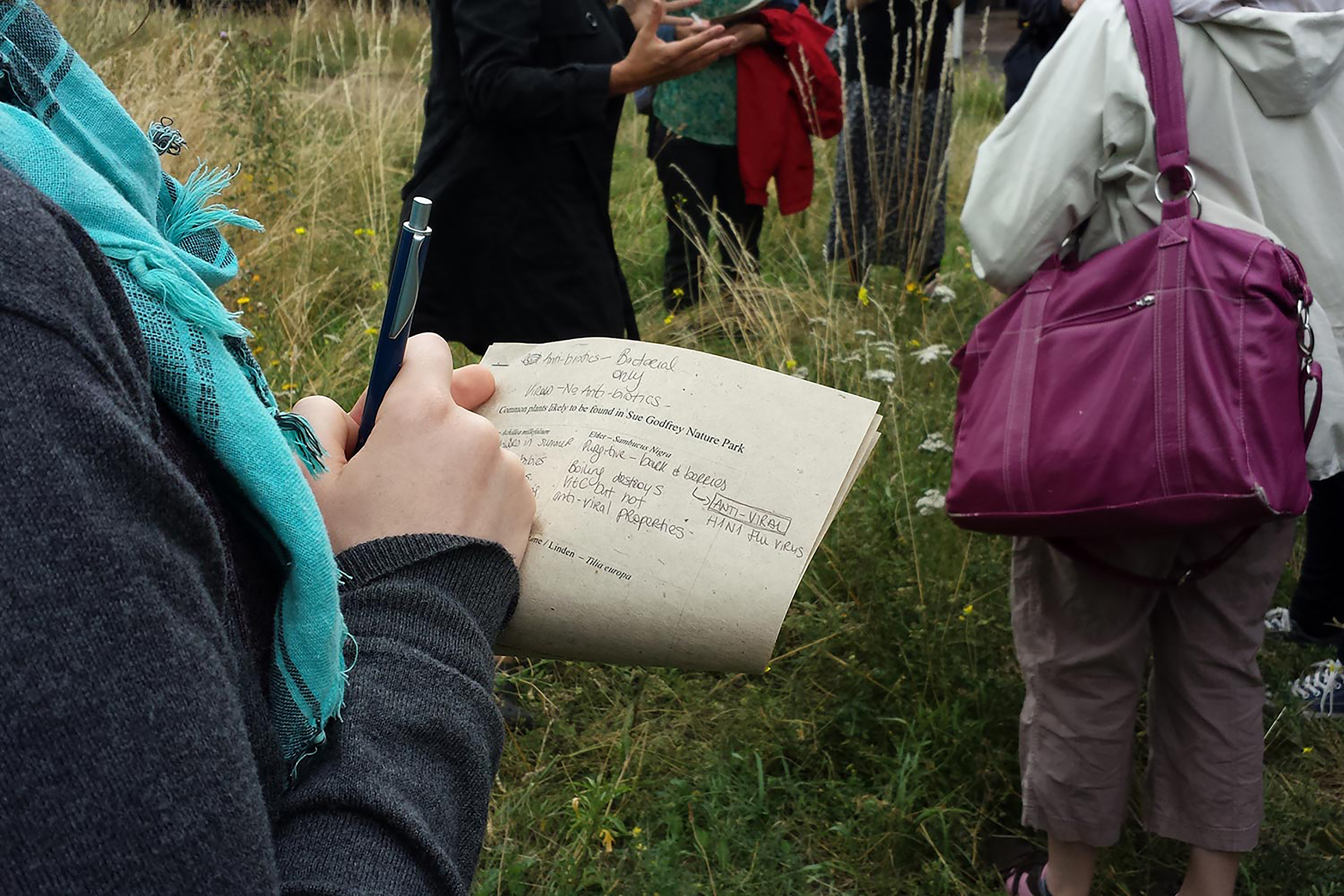 A woman holding a piece of lined paper with writing on it, standing in a field.