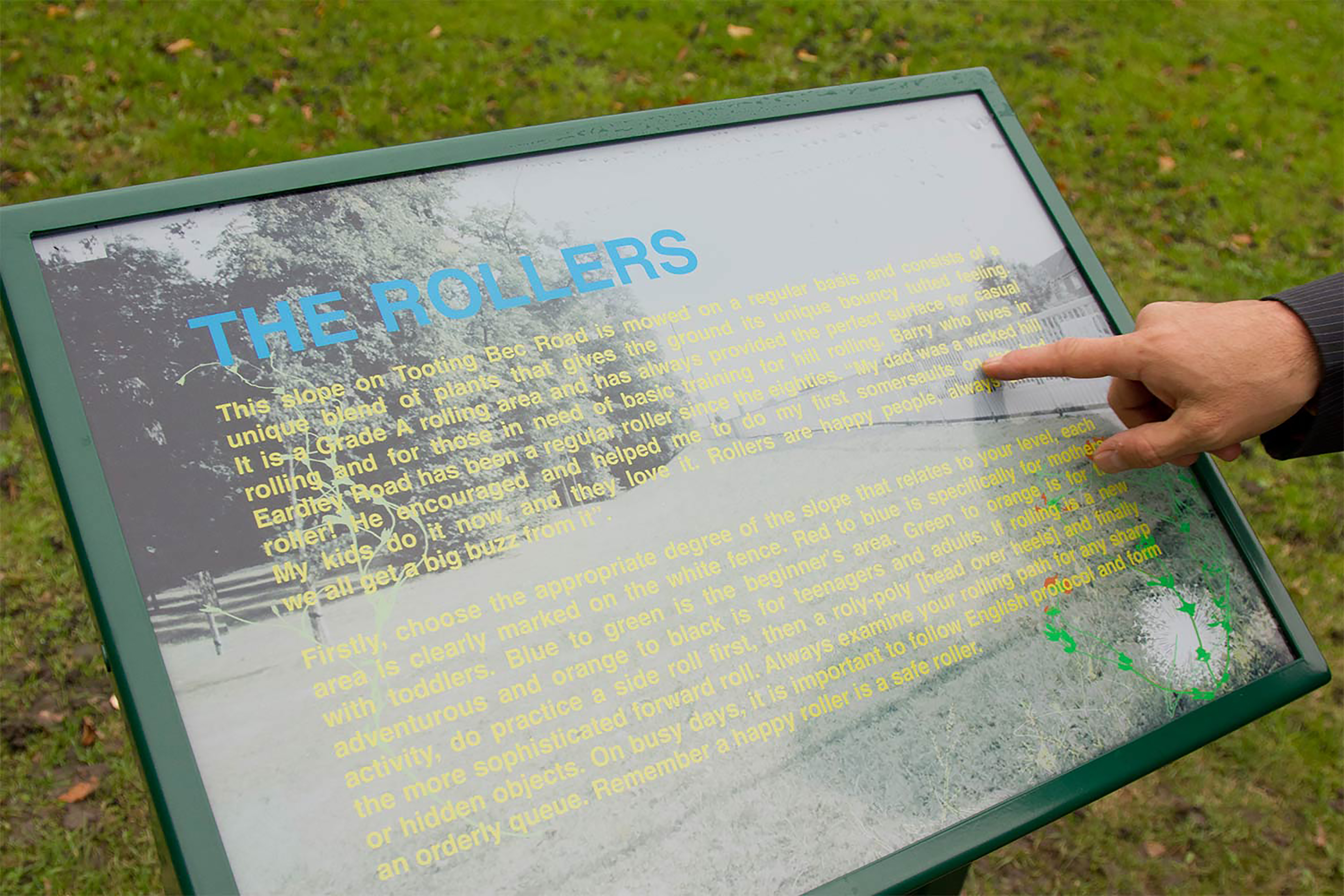 A person point to a green sign in a park with a large informational text section.