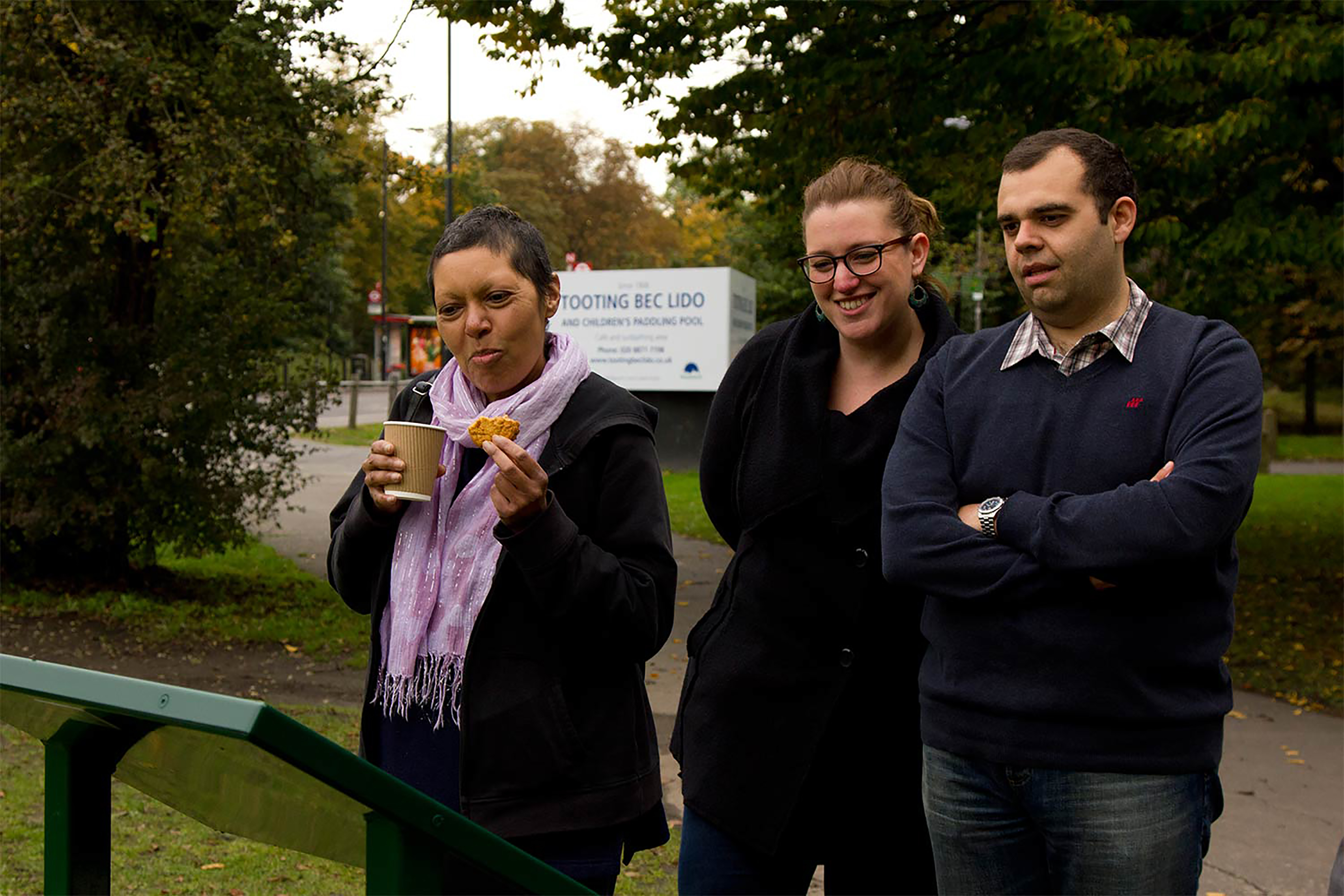 Three people standing together reading a green sign in a park.