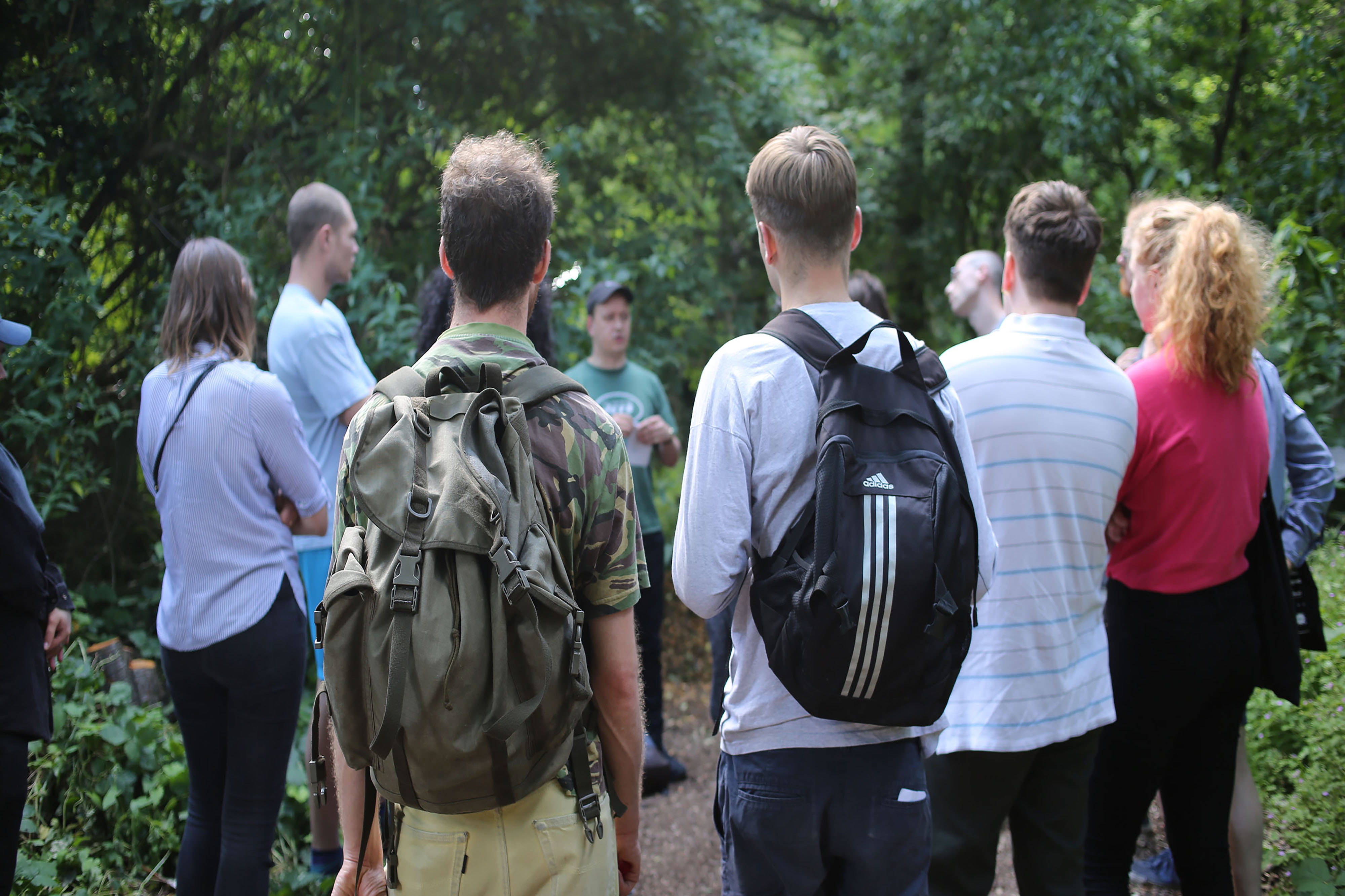 A group of people standing in a circle wearing backpacks in a forest.