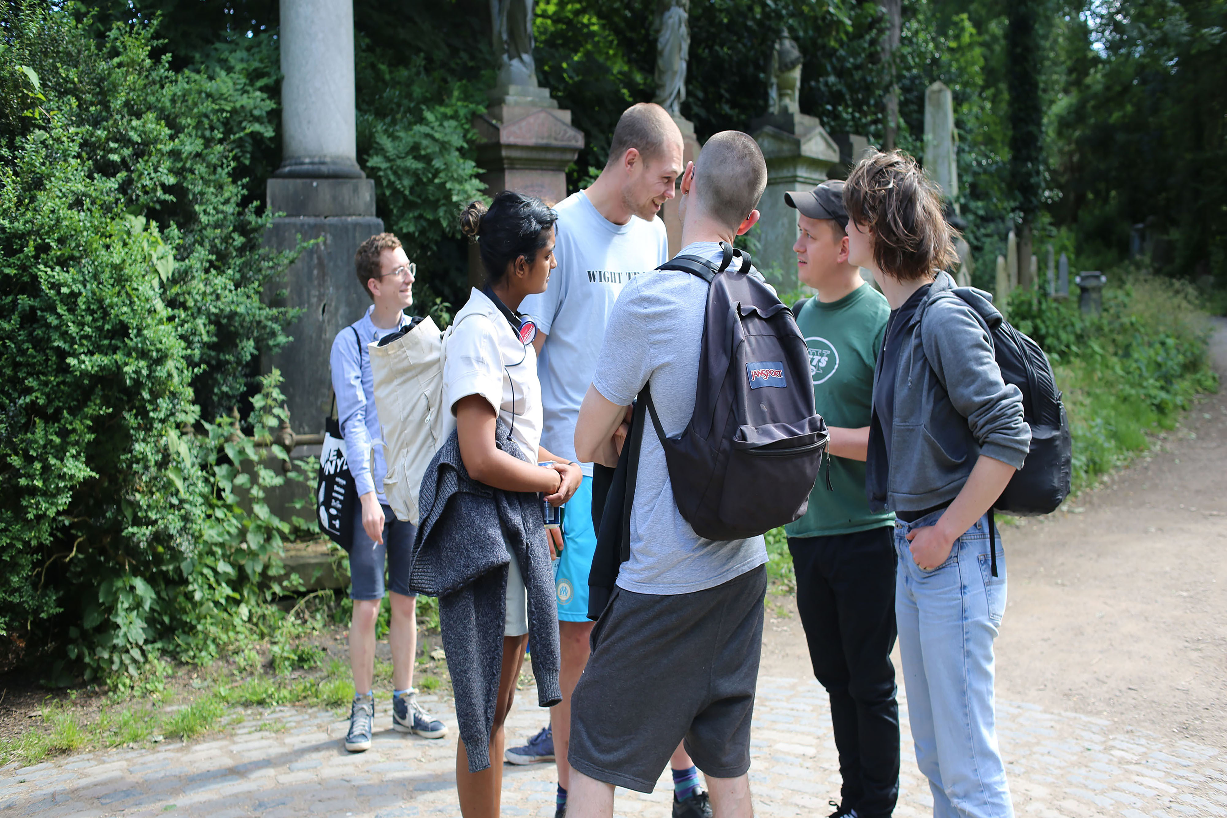 A group of people standing in a circle wearing backpacks in a forest.