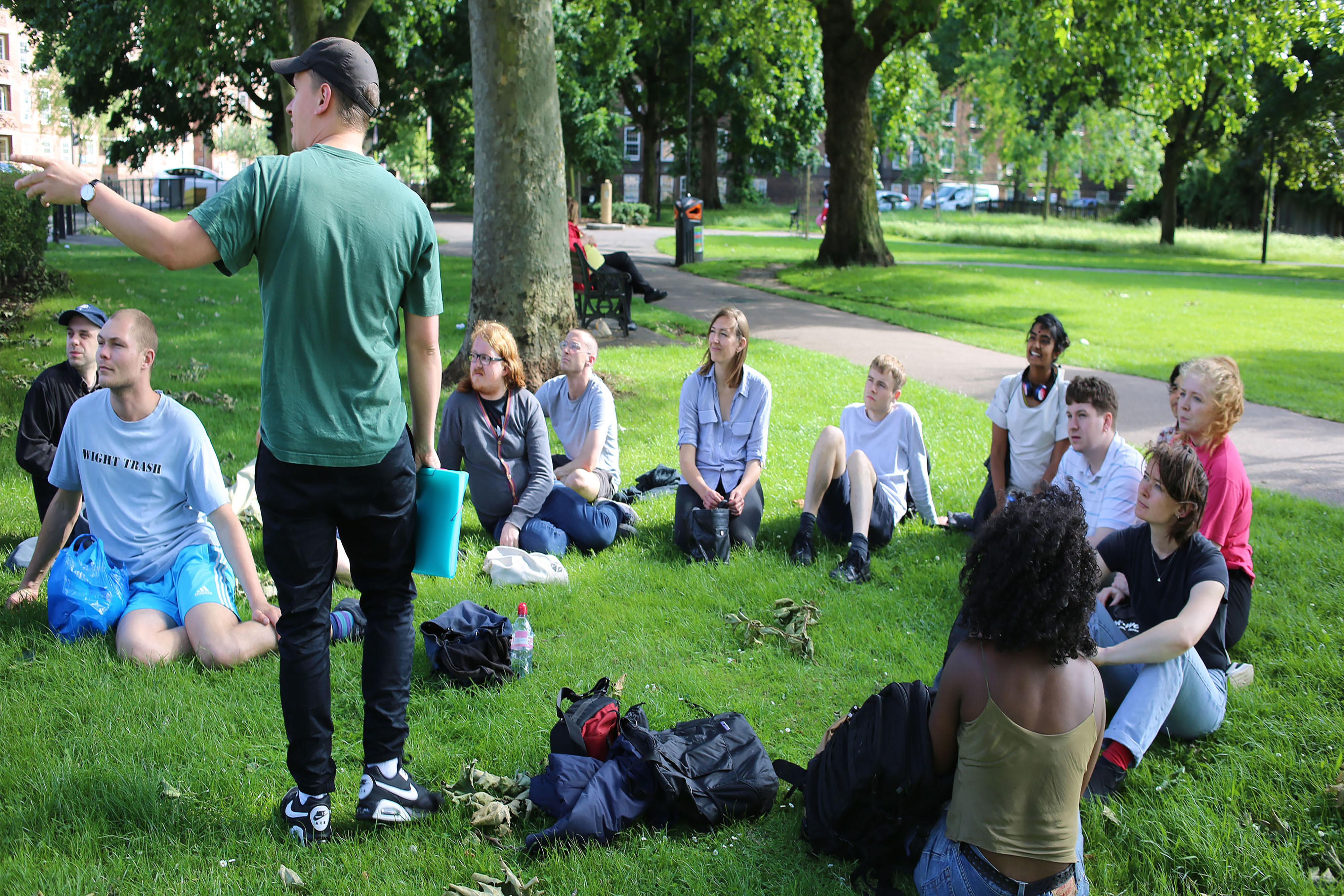 A group of people sitting in a circle watching someone speak in a forest.