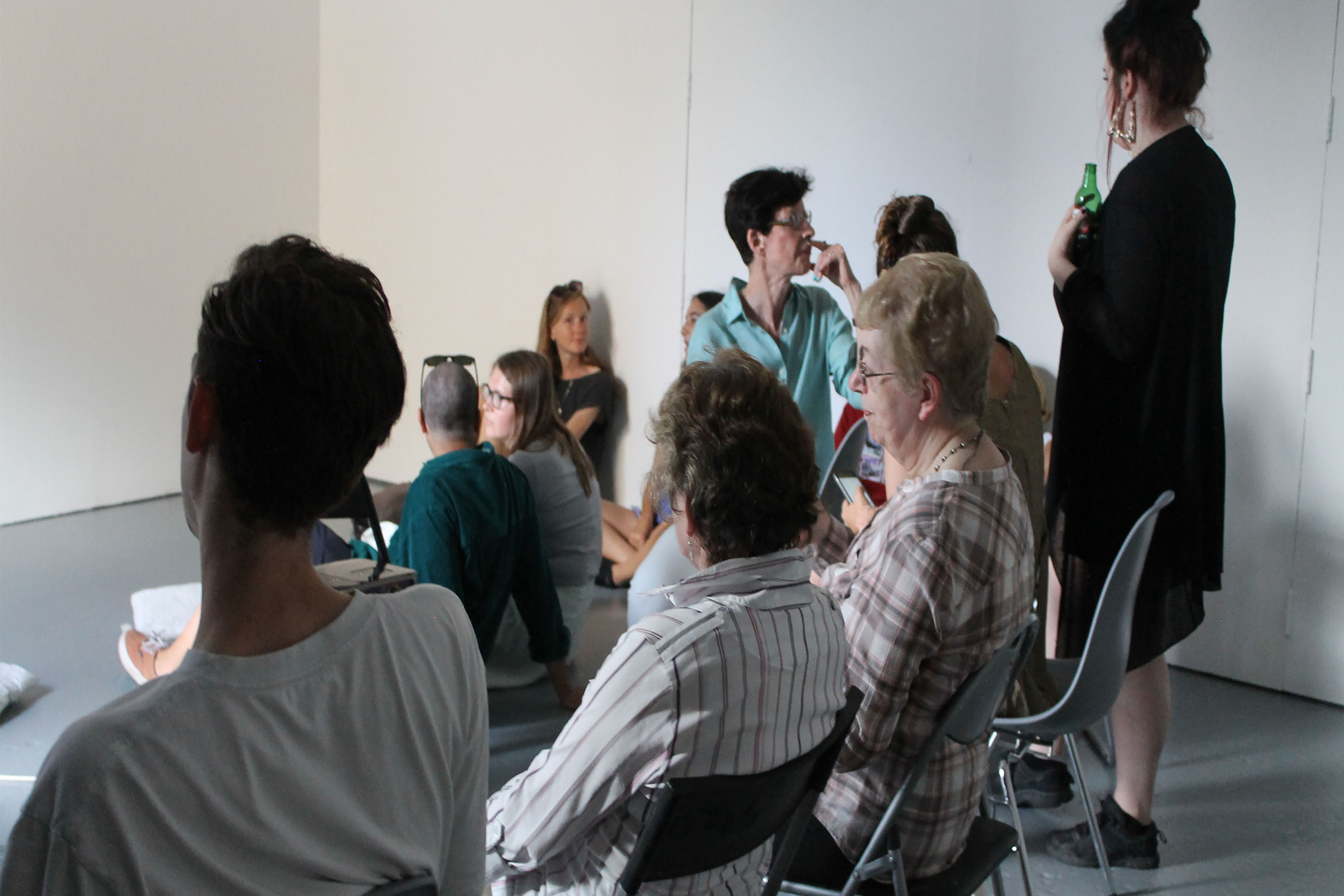 A group of people sitting in a circle on chairs in a white room.