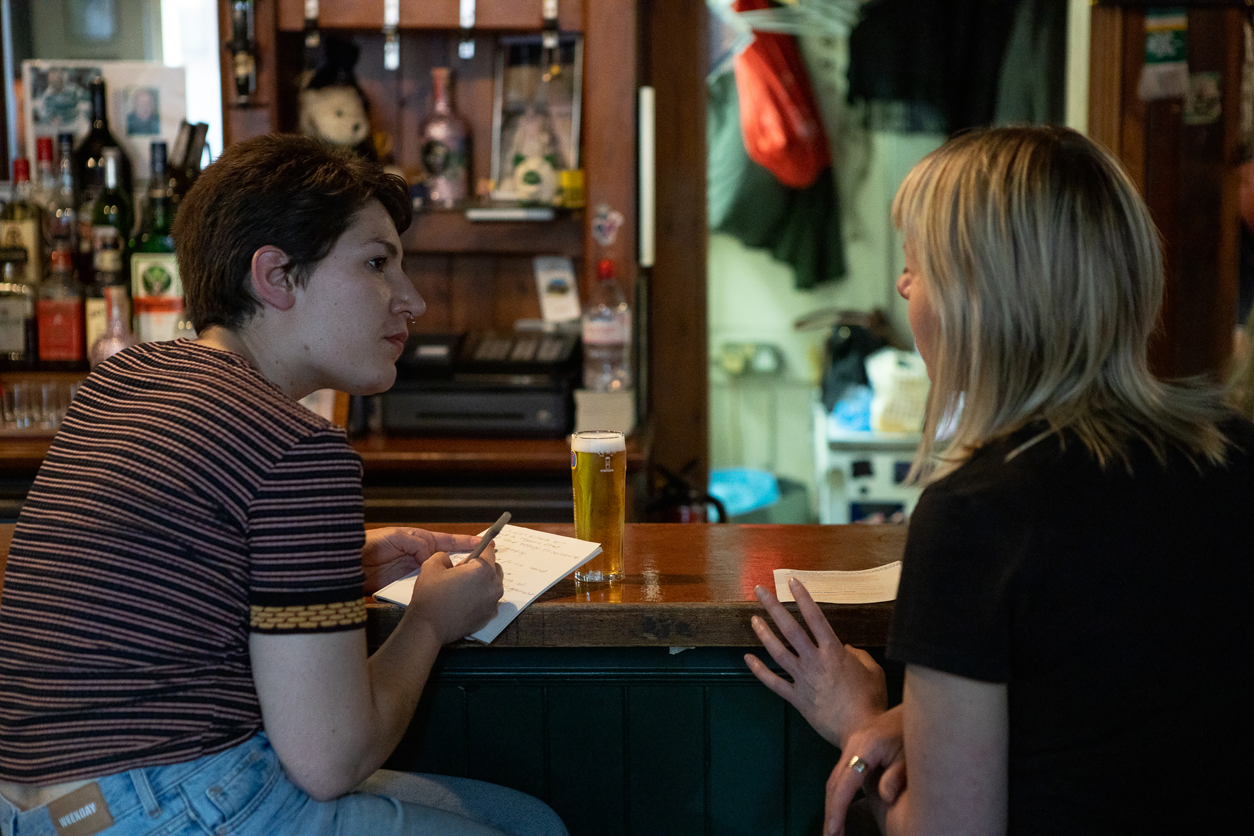 A photograph of two women talking at a bar.