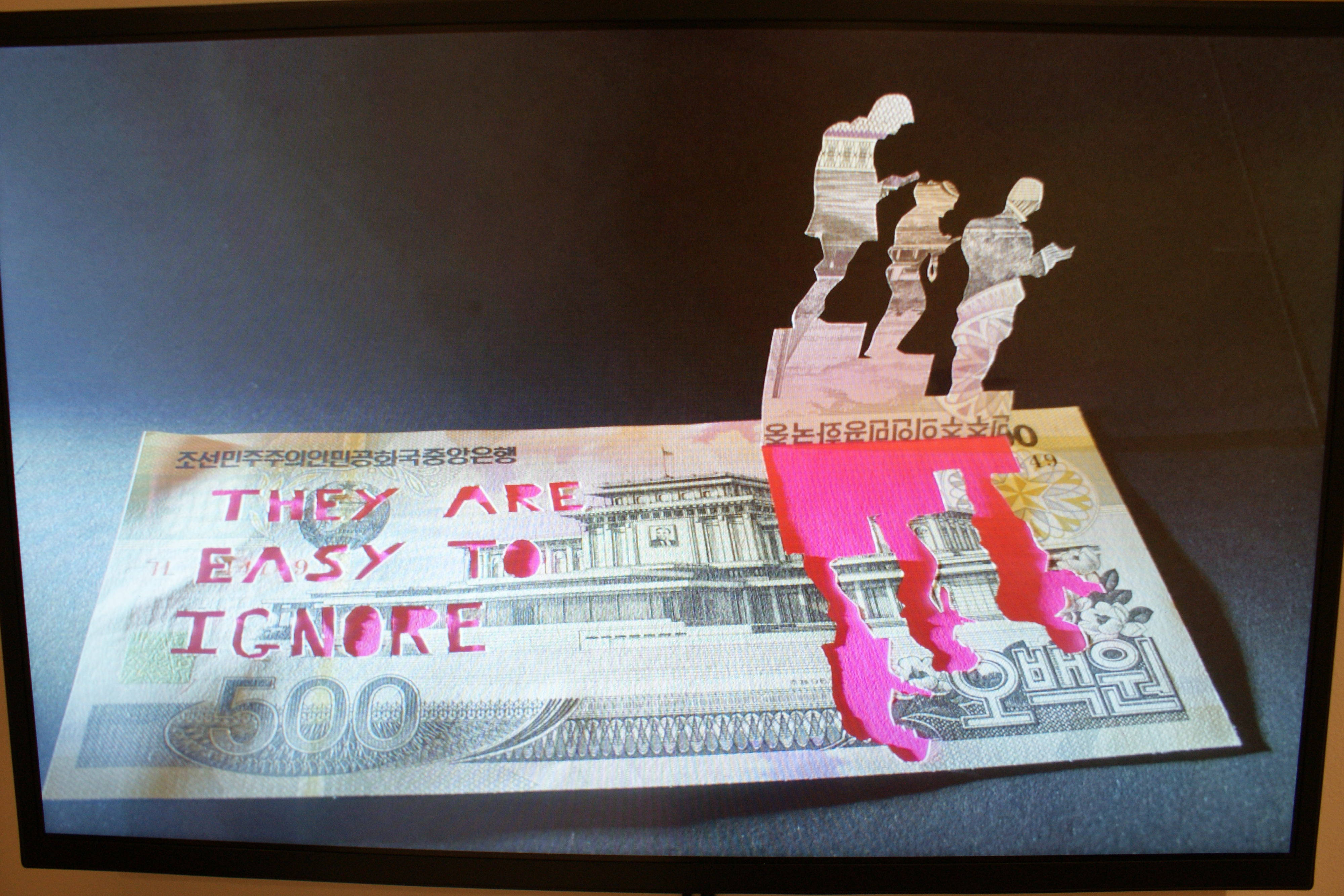 A photograph of a bank note on screen with text intricately cut into it that reads "They Are Easy To Ignore".