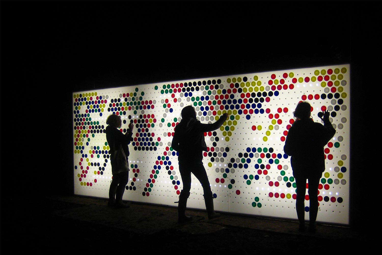 A photograph of people rearranging colourful circles on a white box light display.