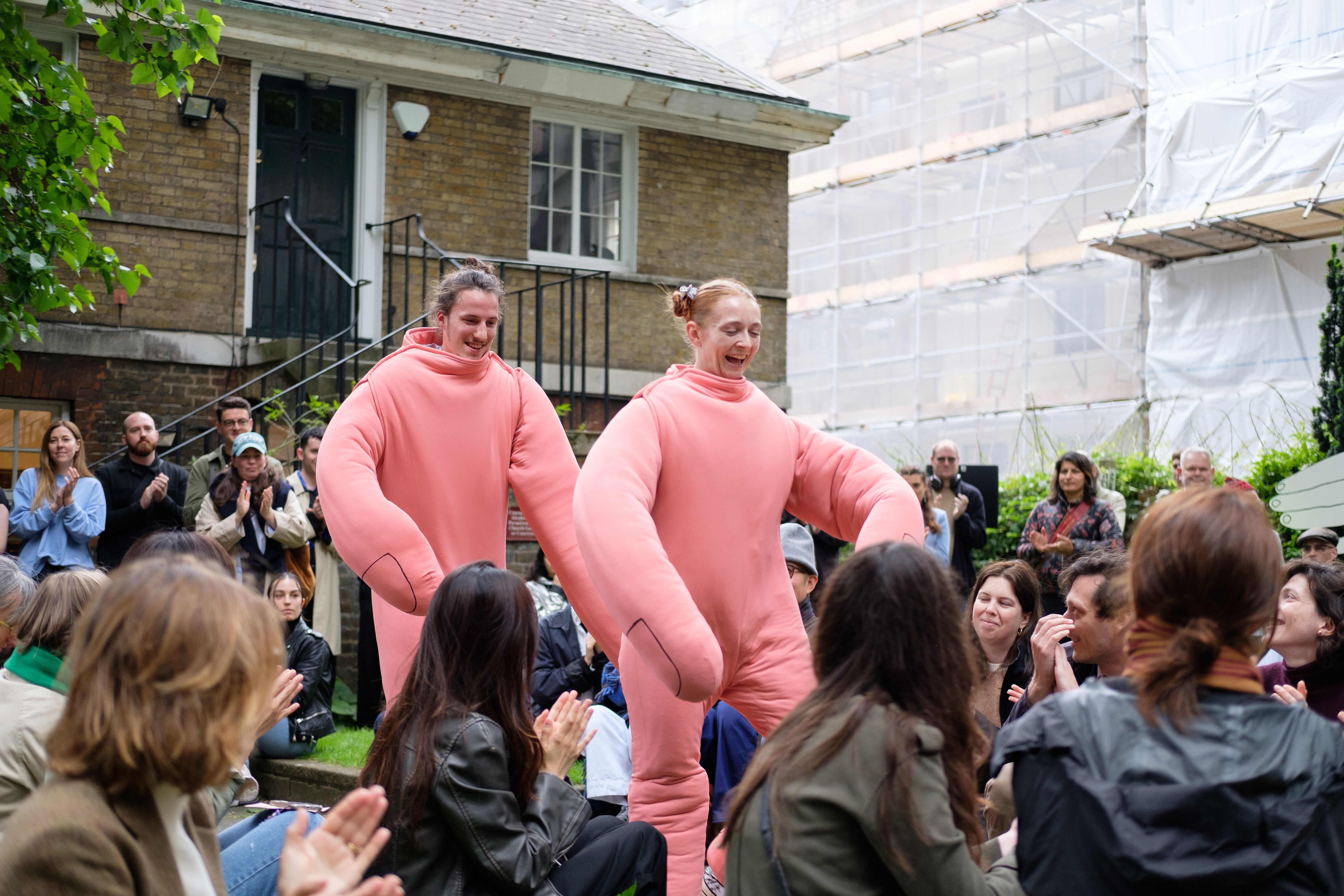 Two dancers dressed as hands walking through a crowd of people in a garden space.