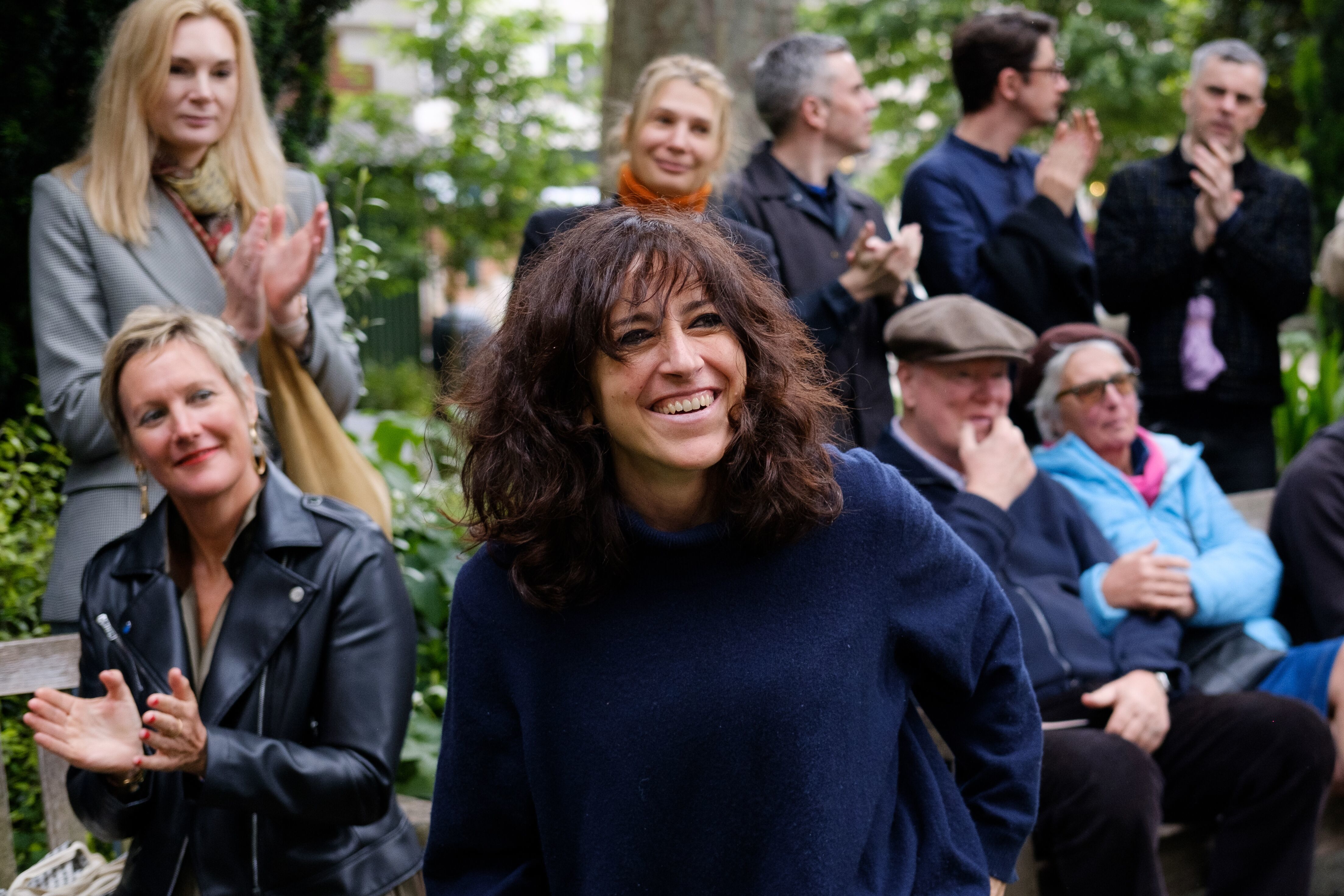 Adelaide Cioni being applauded by a crowd of people in a garden.