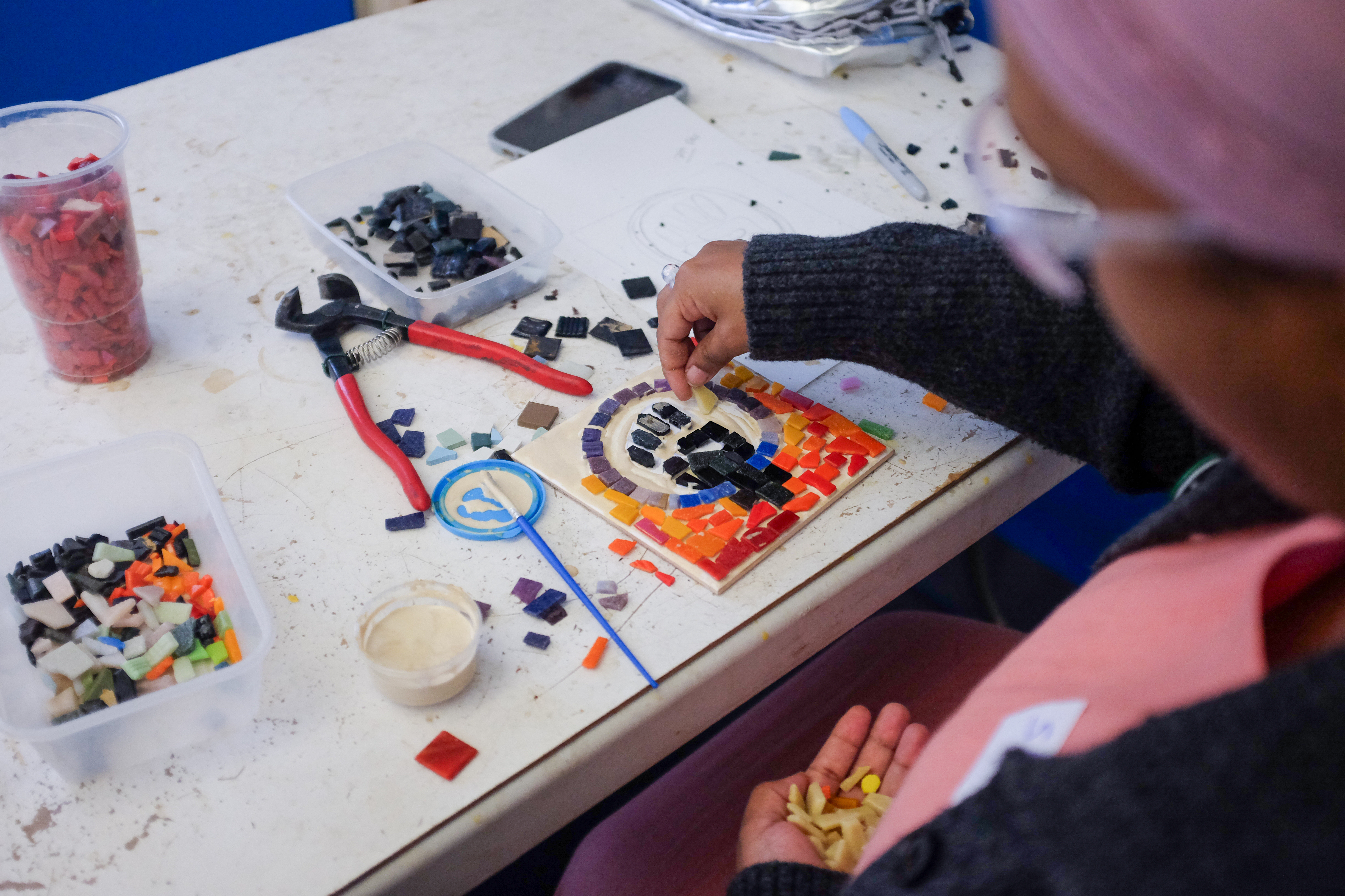 An over the shoulder photo of Sahra Hersi assembling a small mosaic showing the symbol of a feminist fist.