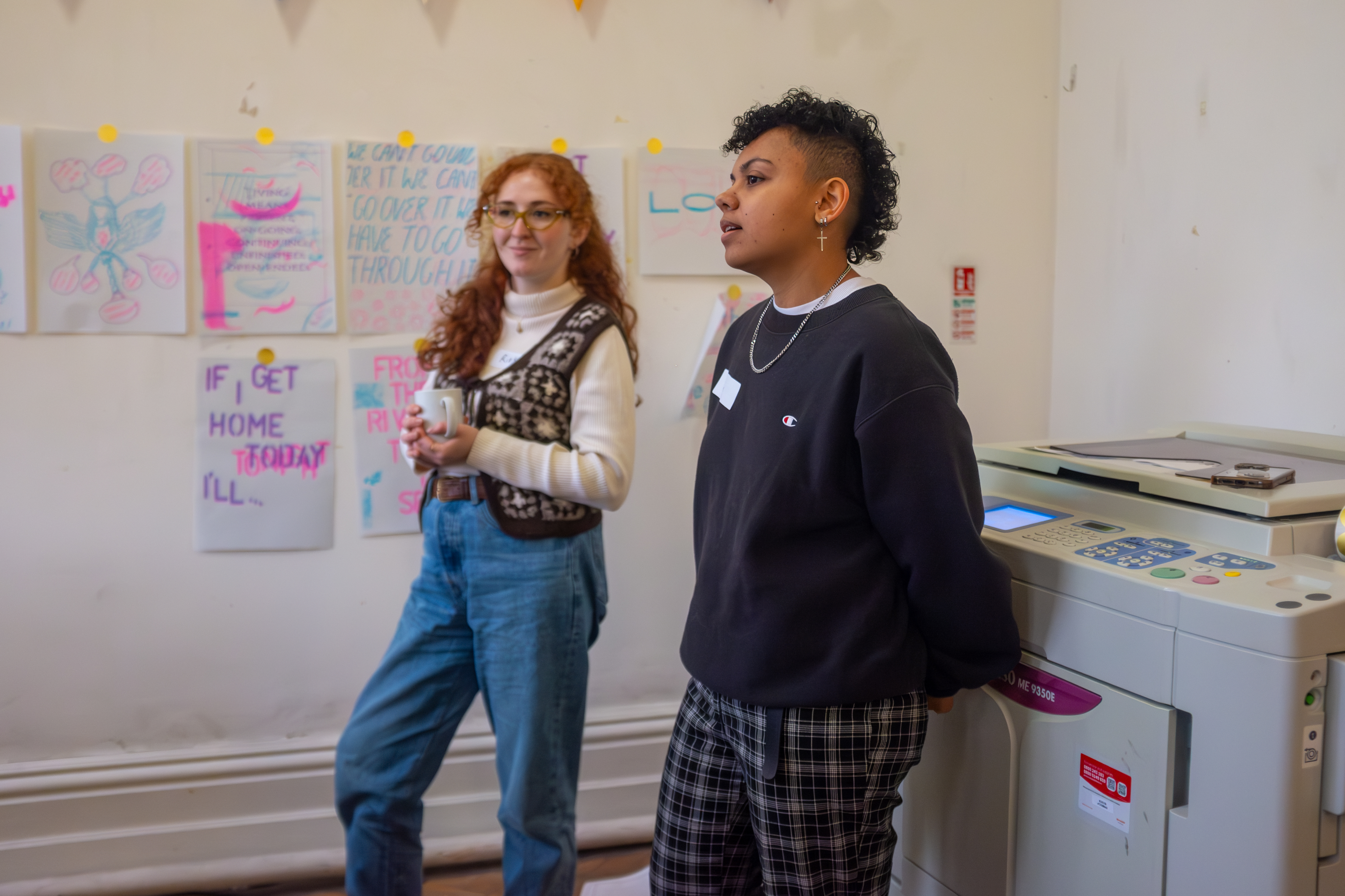 Two women in front of a large risograph printer talking