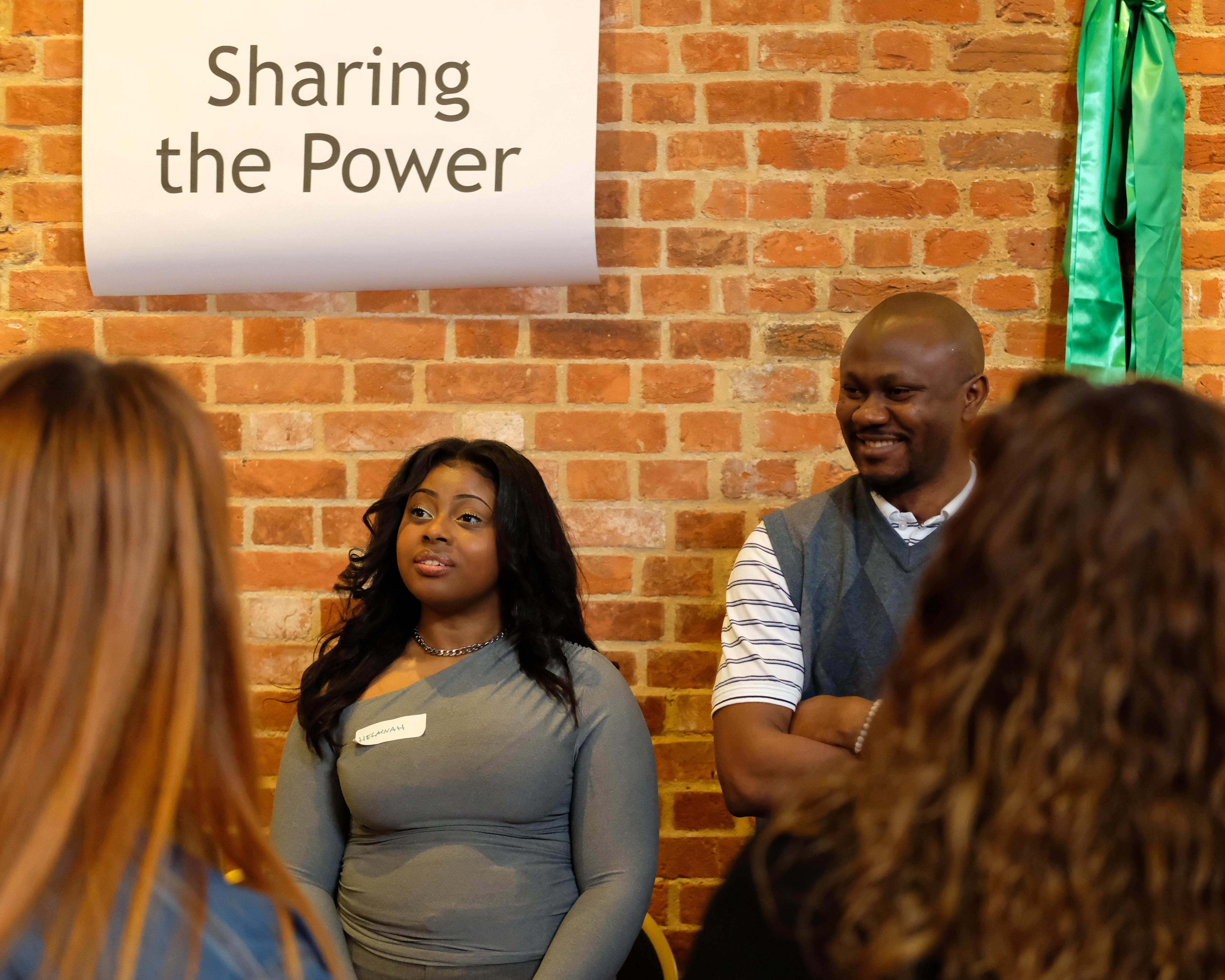 Two people stand in front of a sign that says 'Sharing the Power'