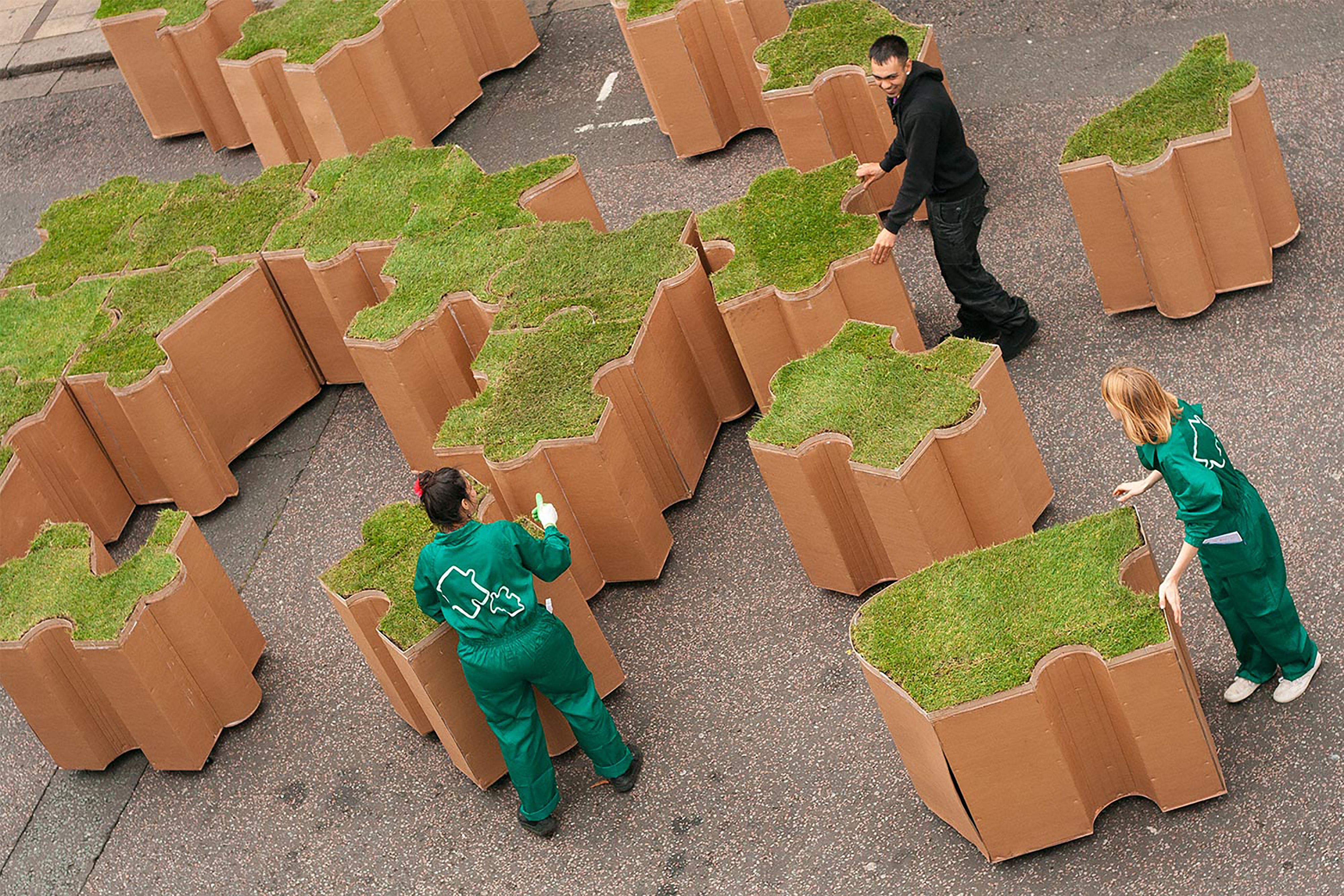 Three gardeners assembling terracotta blocks of turf in the shape of a jigsaw puzzle.