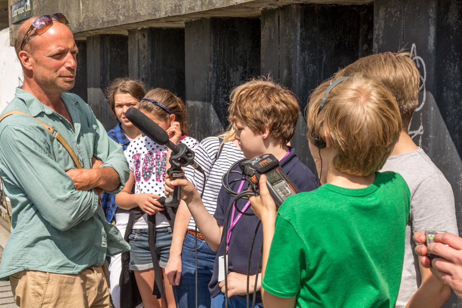 A group of children and adults recording and filming a man outdoors in a park.
