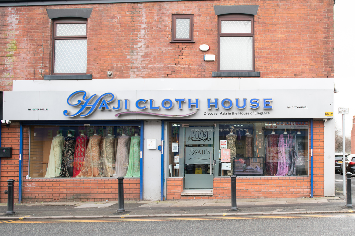 A high street shop with a window full of coloured kamees with the sign reading “Haji Cloth House”.