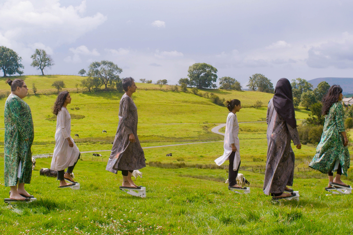 A group of women on exercise steppers in a field holding white papers, all wearing different coloured Khamis.