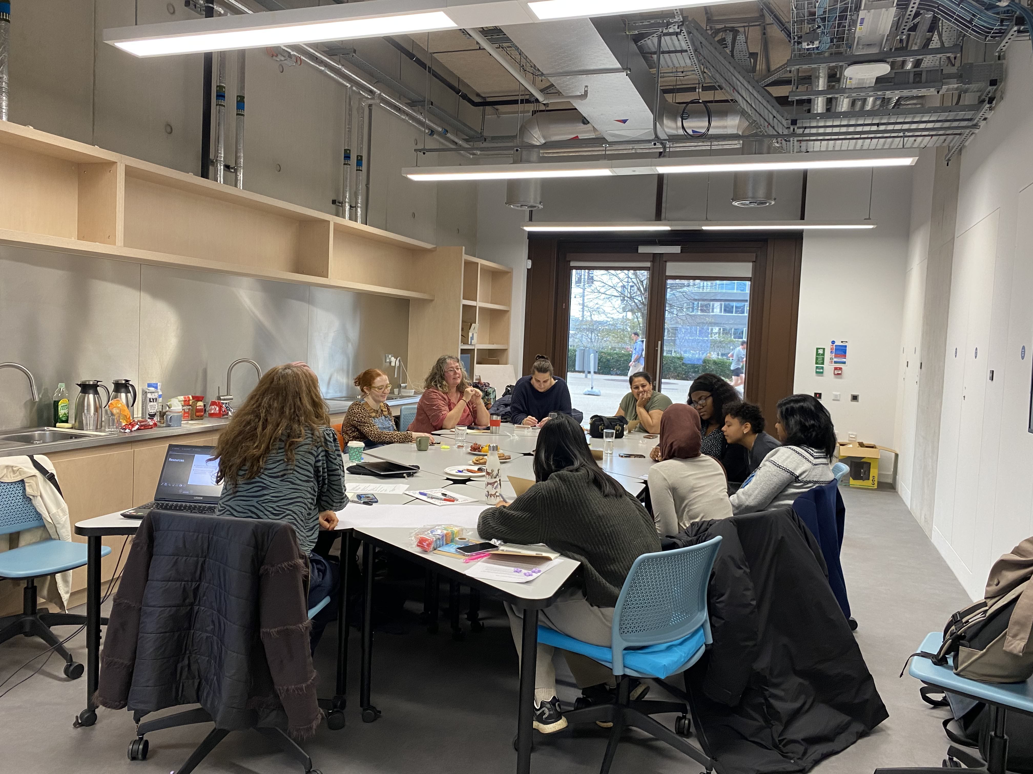 Group of 9 women in discussion around a table in a university room