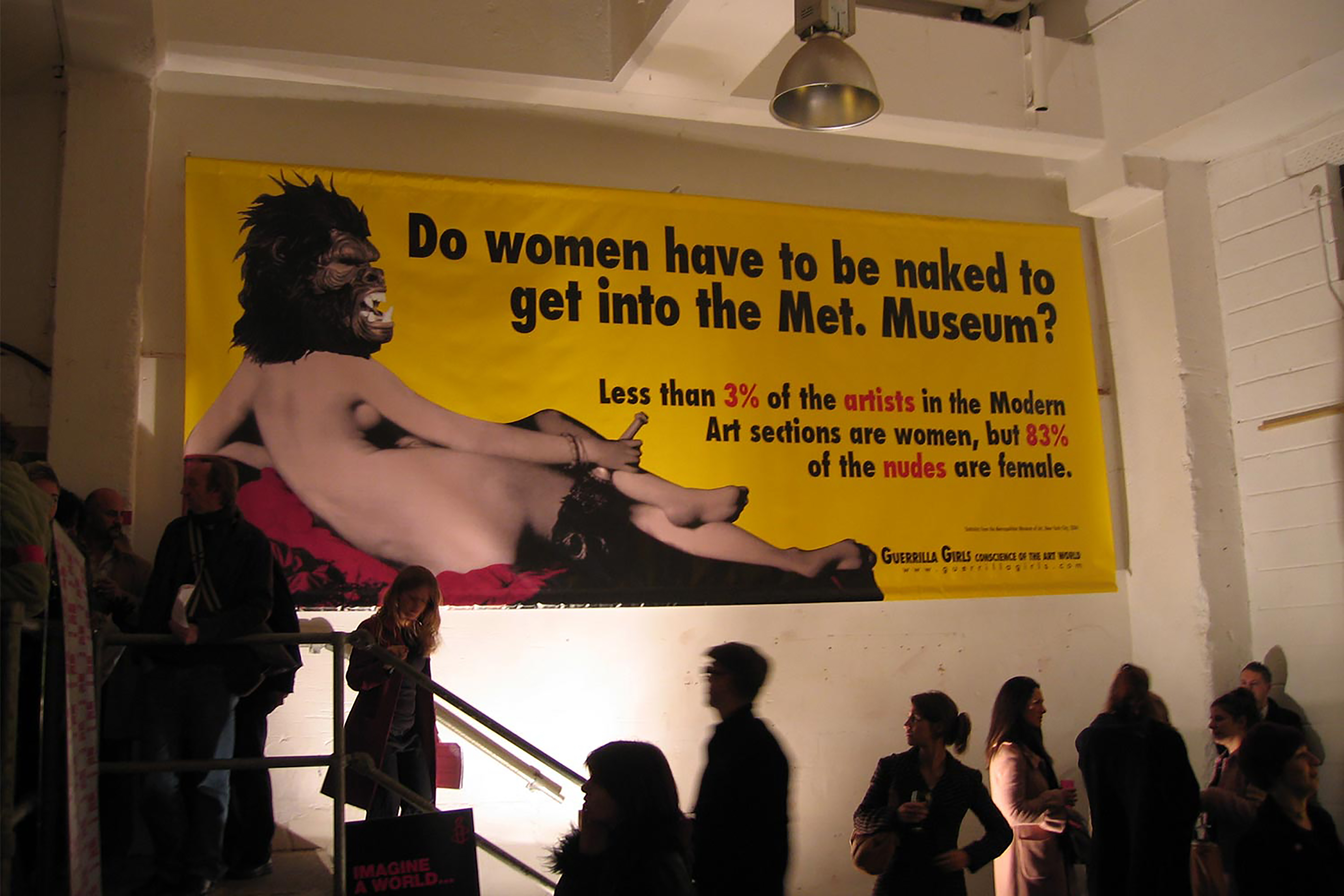 A large sign hanging above a gallery stairwell that reads' Do women have to be naked to get into the Met. Museum?'