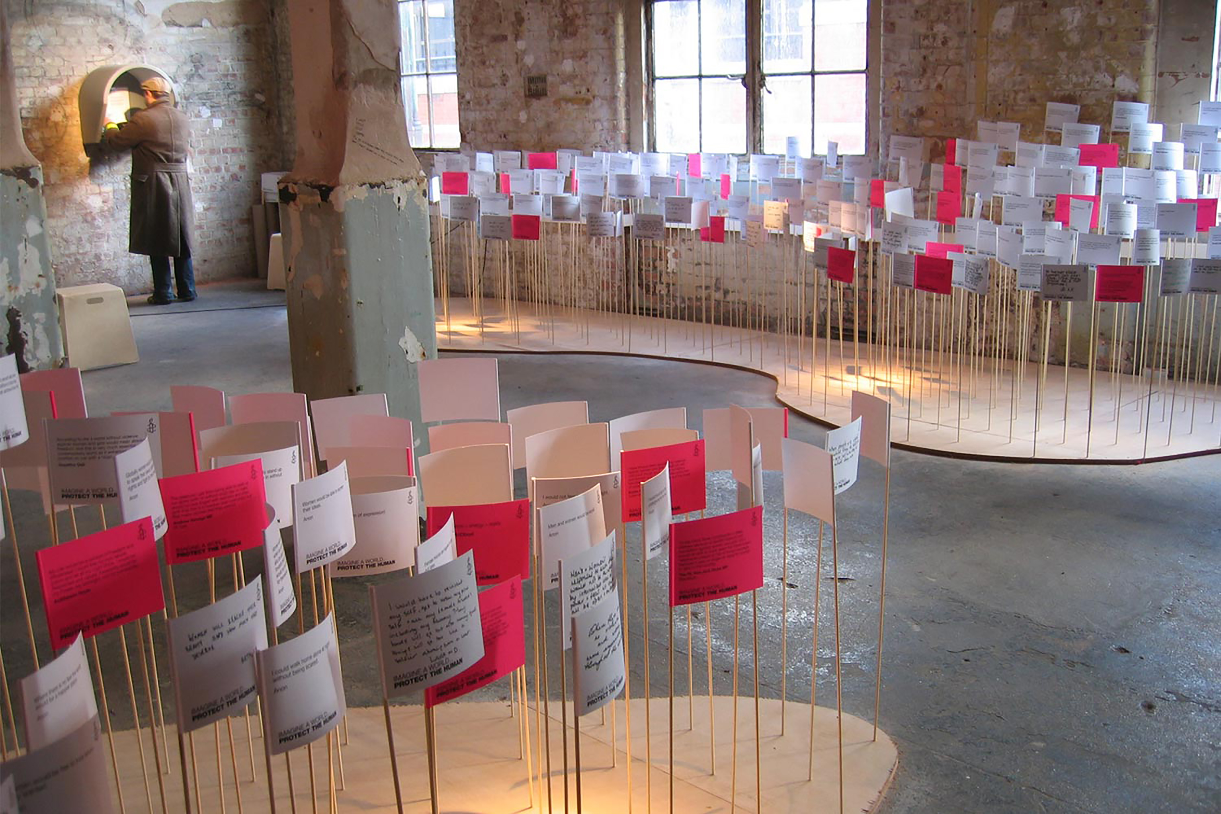 A photograph of warehouse floor occupied with red and white flags covered in text sprouting from the ground.