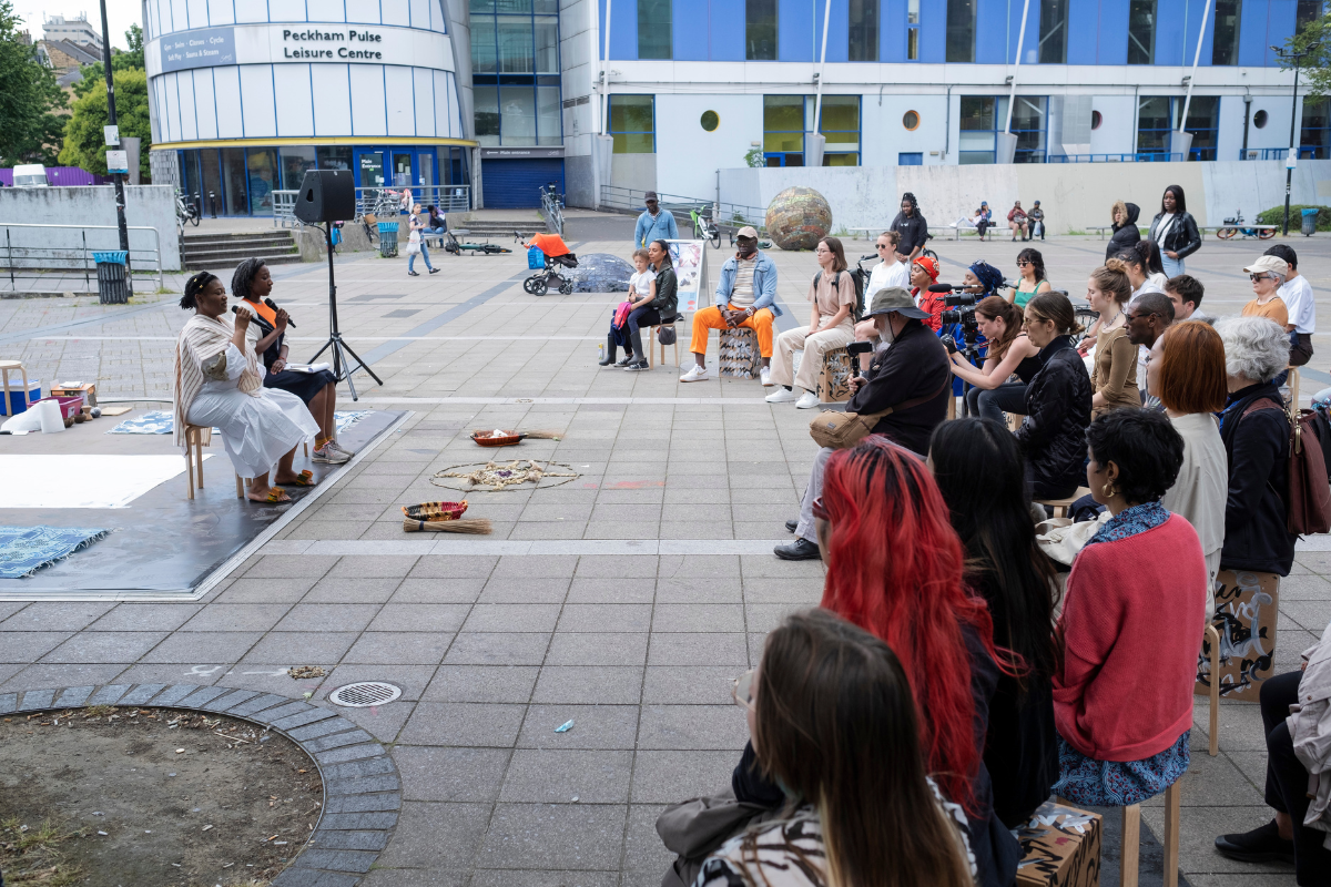 Two women holding a microphone speaking to a group of people on a street.