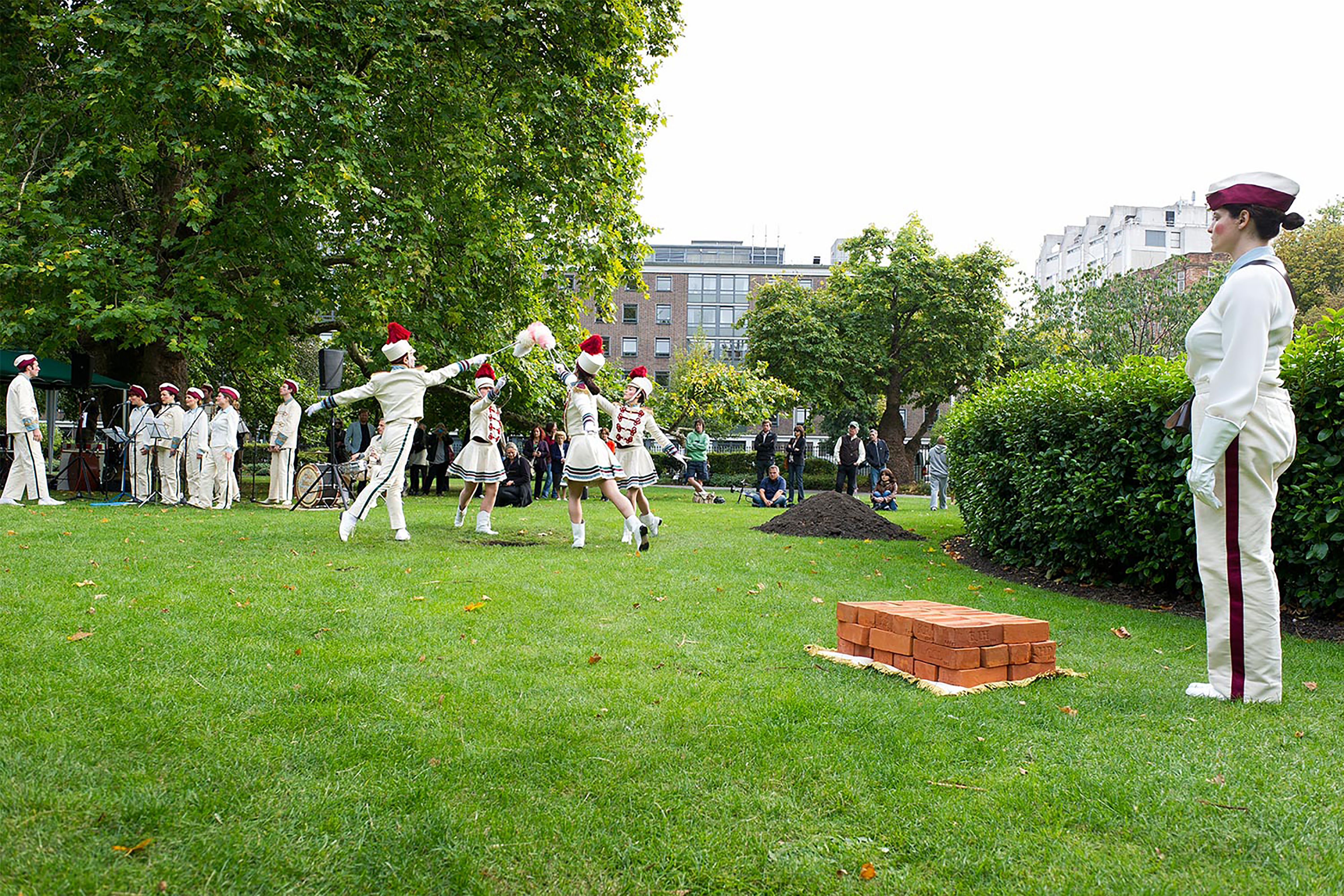 A photograph of a woman in a parade outfit stood near a pile of bricks in a park.
