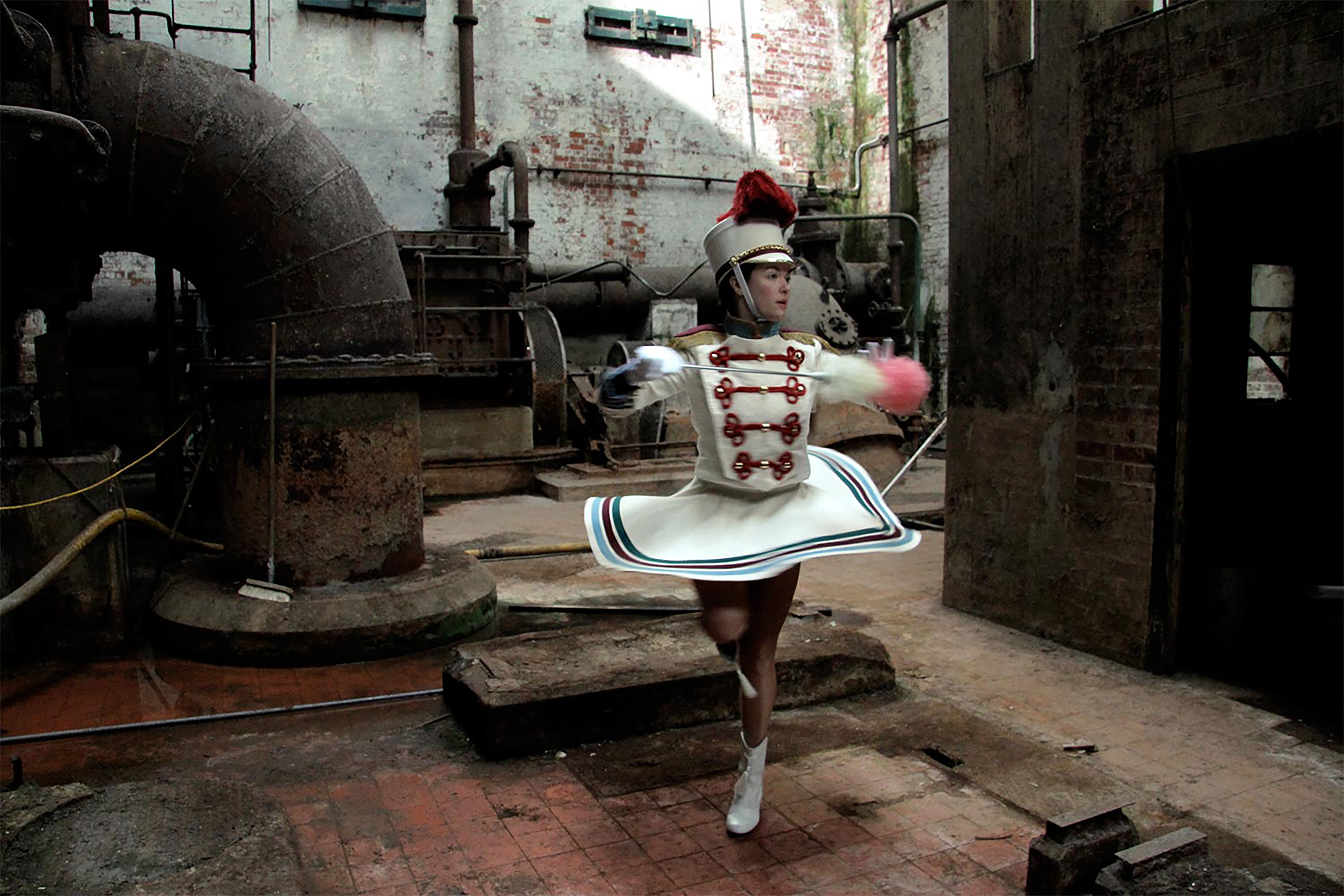 A photograph of performers dancing in a circle in a dark industrial space.