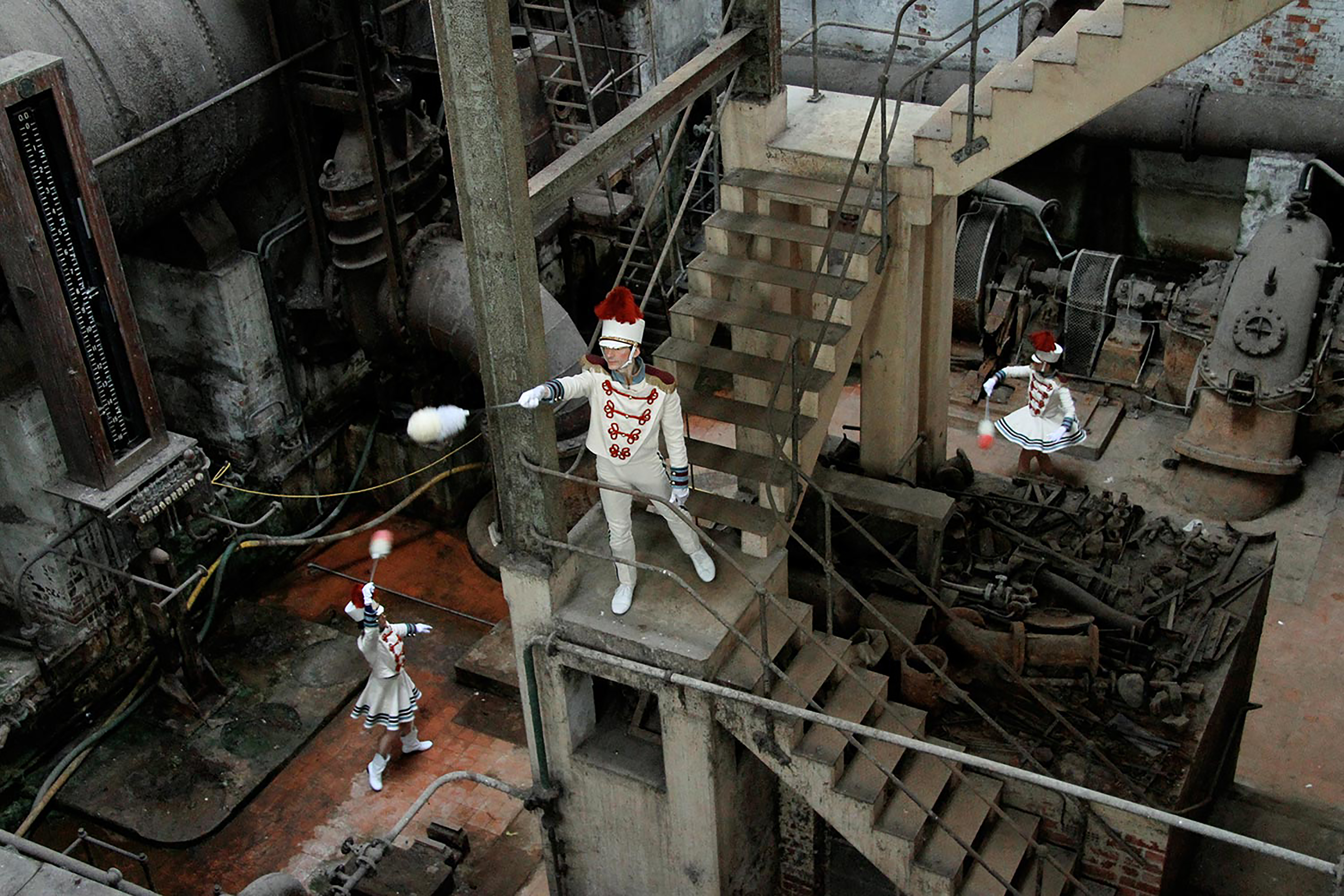 A photograph of performers posing at different heights in a dark industrial space.