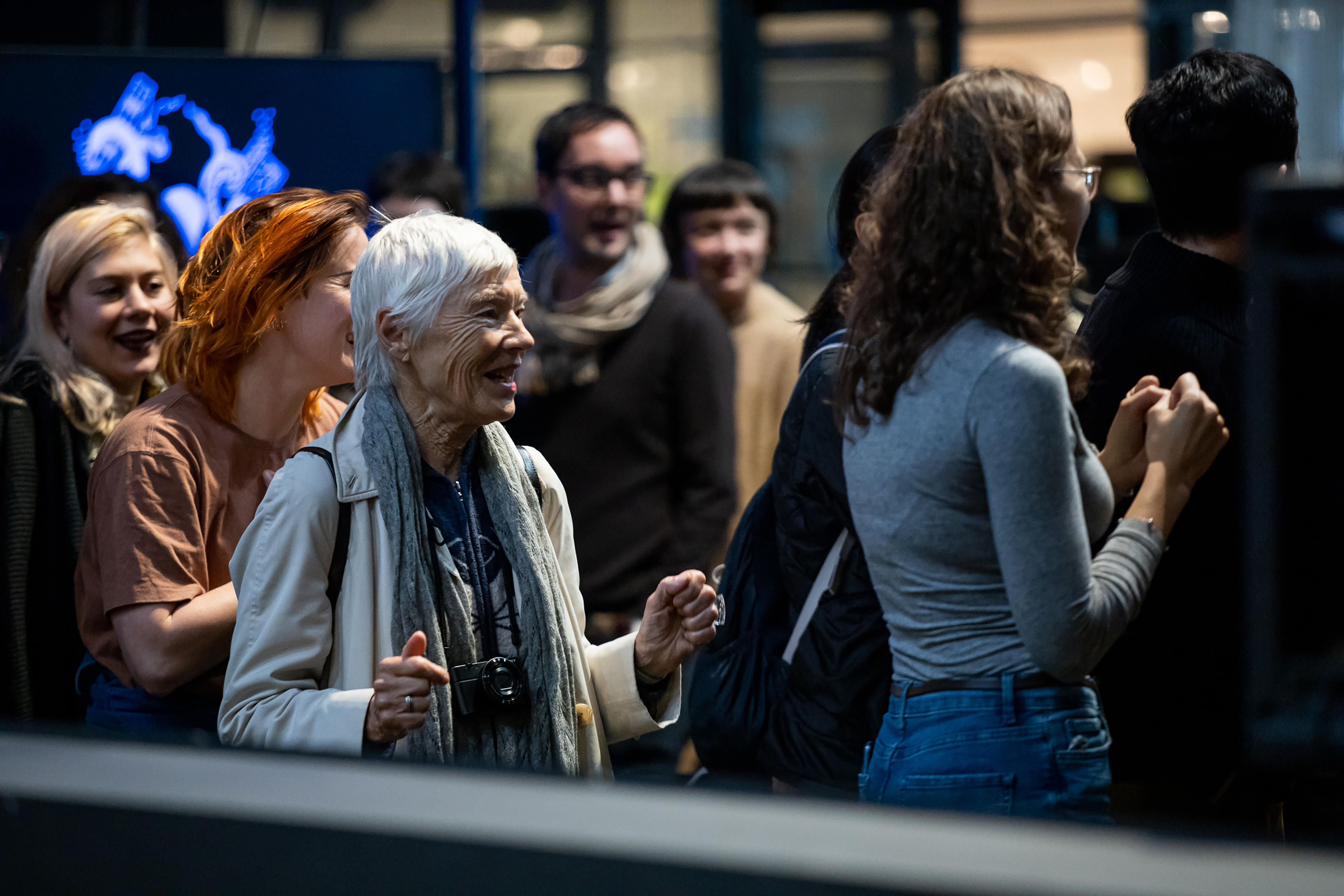A group of people standing in queue, behind a grey bar, all smiling and lifting their arms in joy.