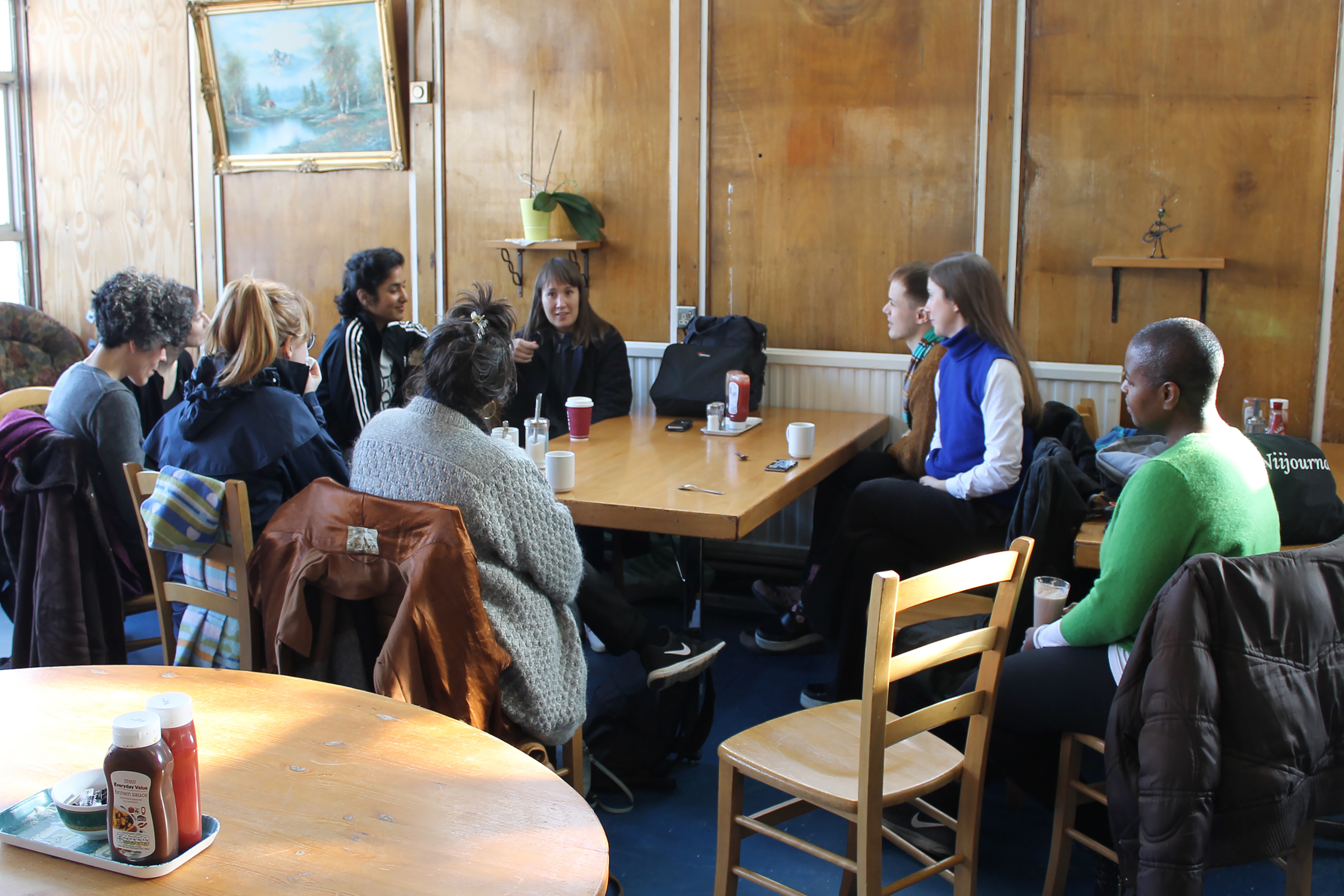 A photograph of a group of people huddled round a table in a dark brown wooden café.
